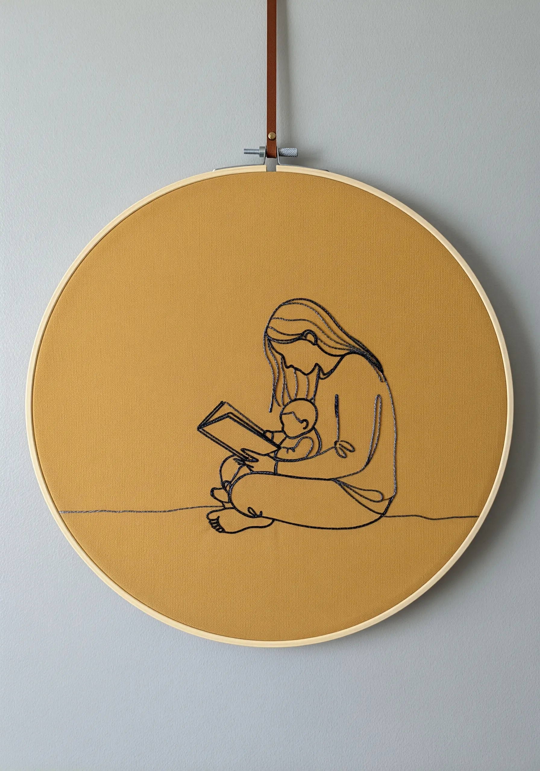 Line art of a mother reading to her baby, stitched in dark thread on a rich mustard-yellow fabric.