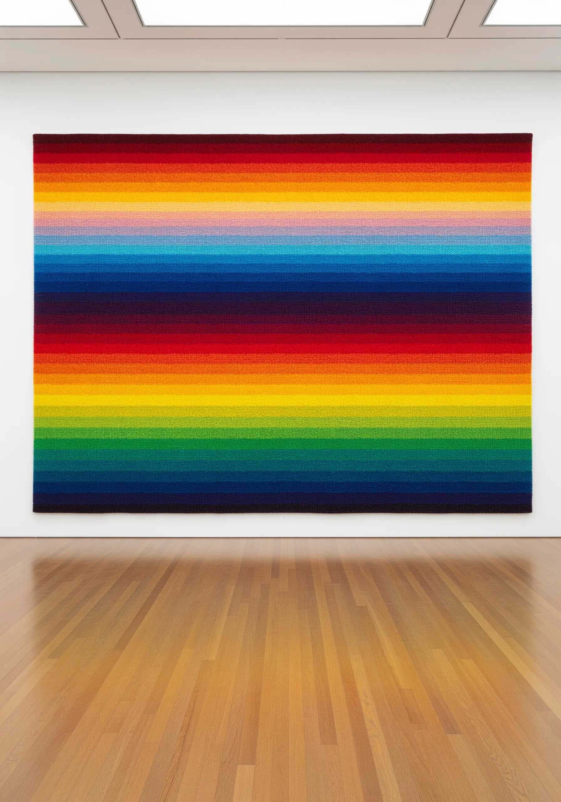 A massive wall tapestry with horizontal stripes of color that form a seamless rainbow gradient.