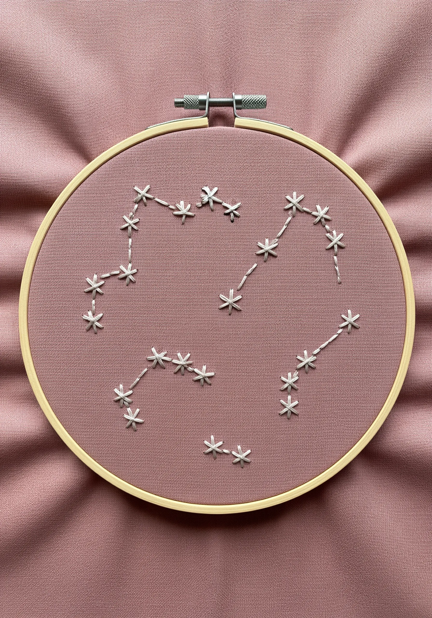 Minimalist constellation patterns embroidered in white thread on a dusty rose fabric.
