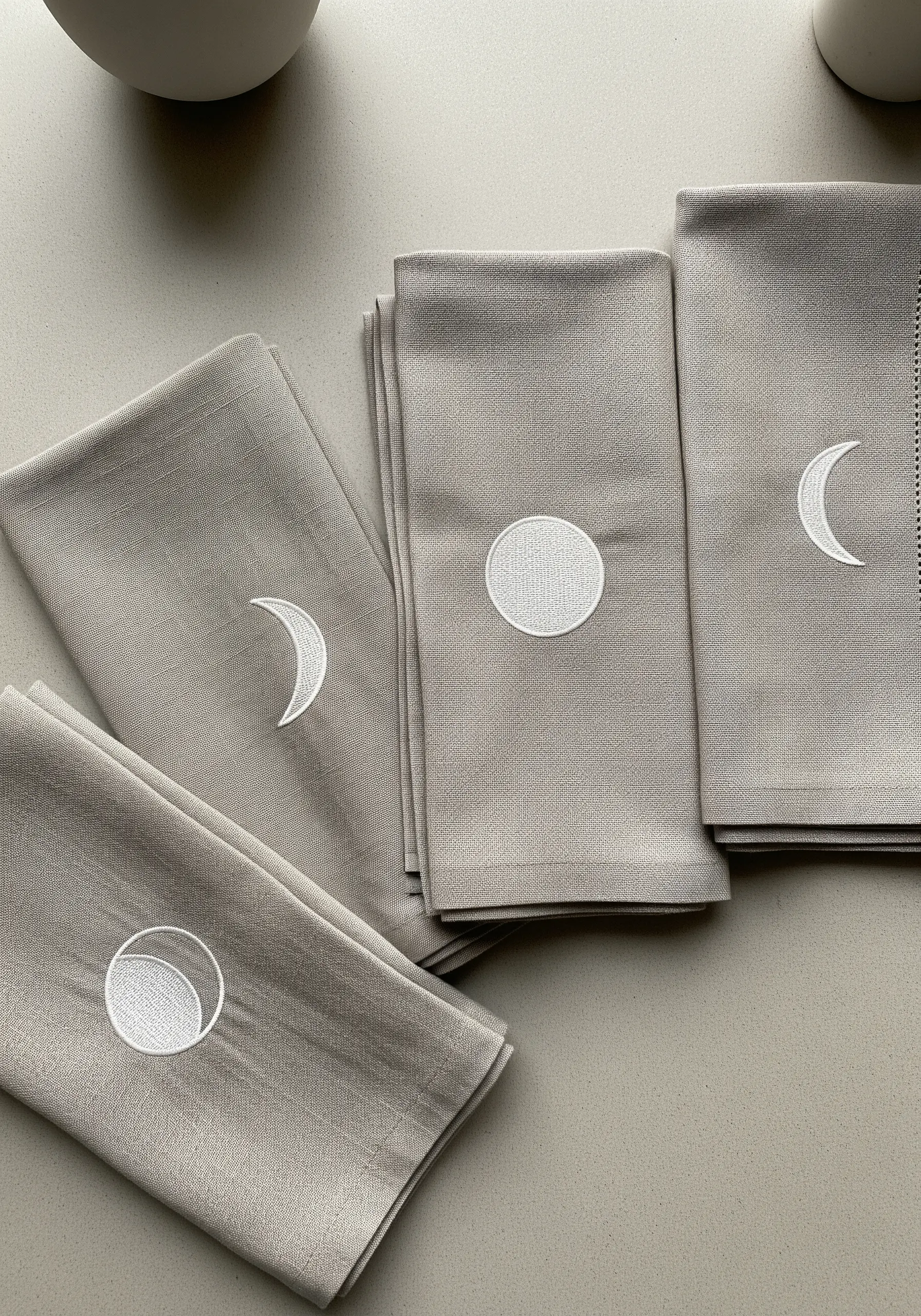 Taupe napkins embroidered with different moon phases in a clean, white satin stitch.