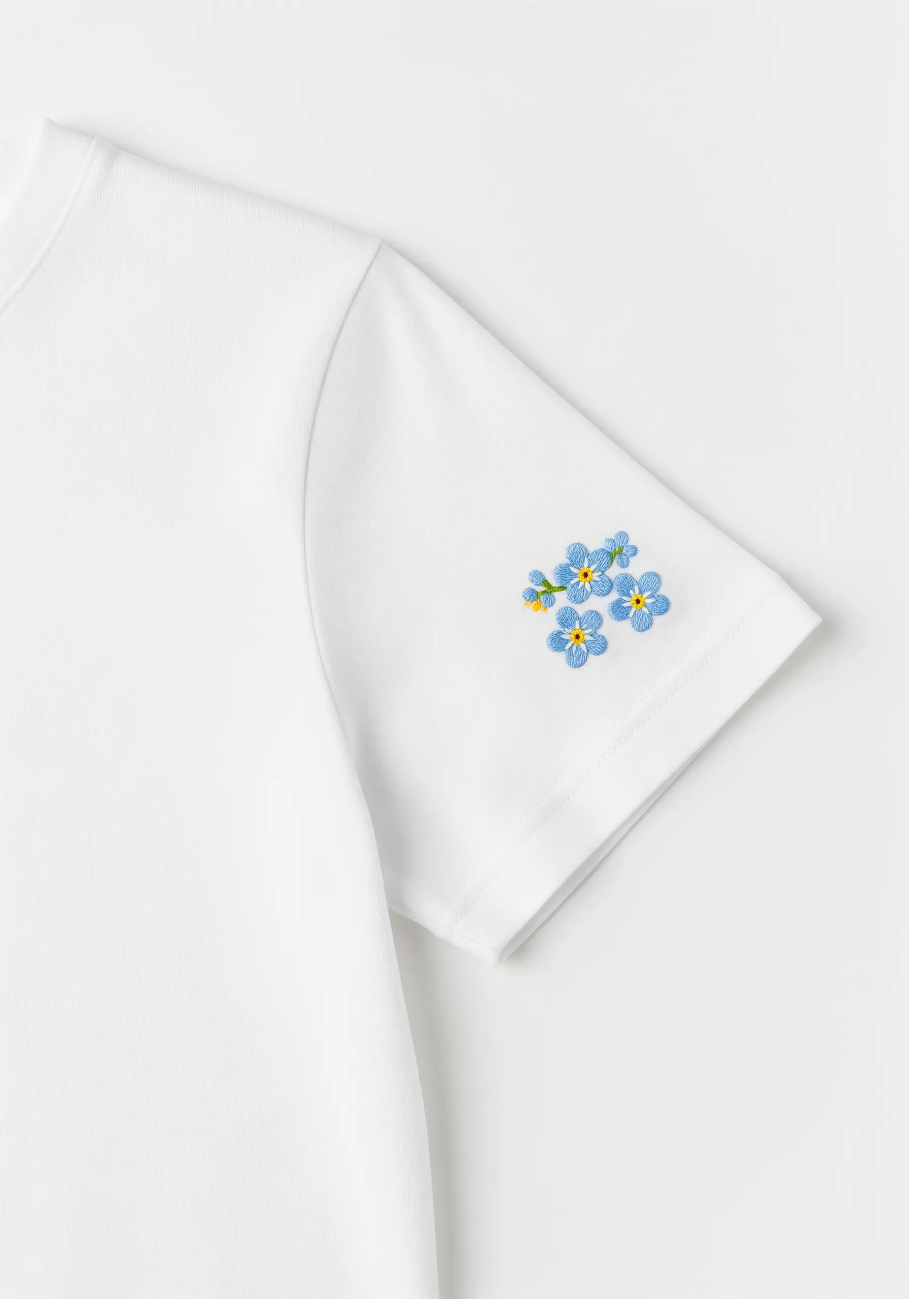 A small cluster of blue forget-me-not flowers embroidered on a sleeve cuff.