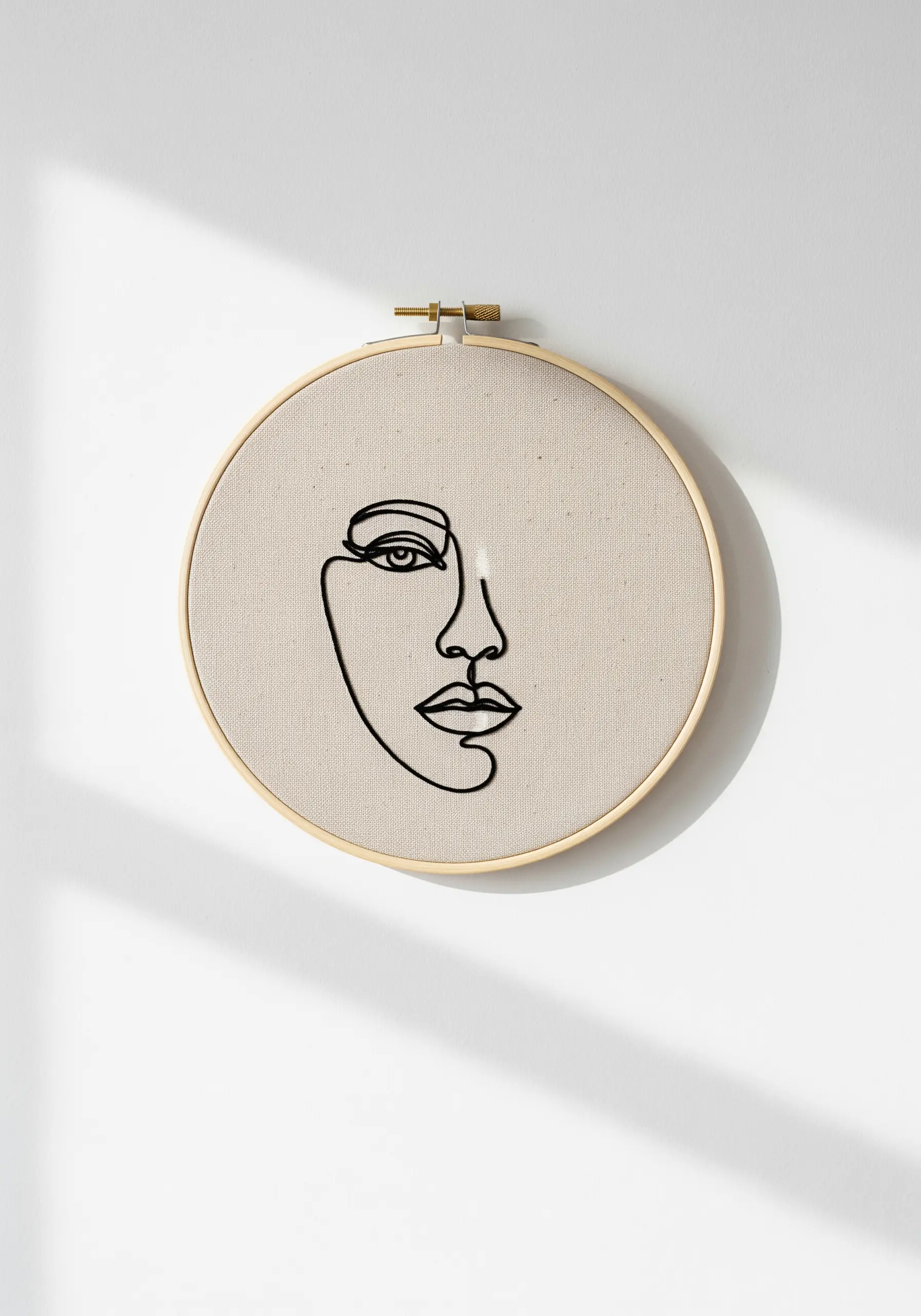 A single black thread creates a continuous line art face profile on beige fabric in a wooden hoop.