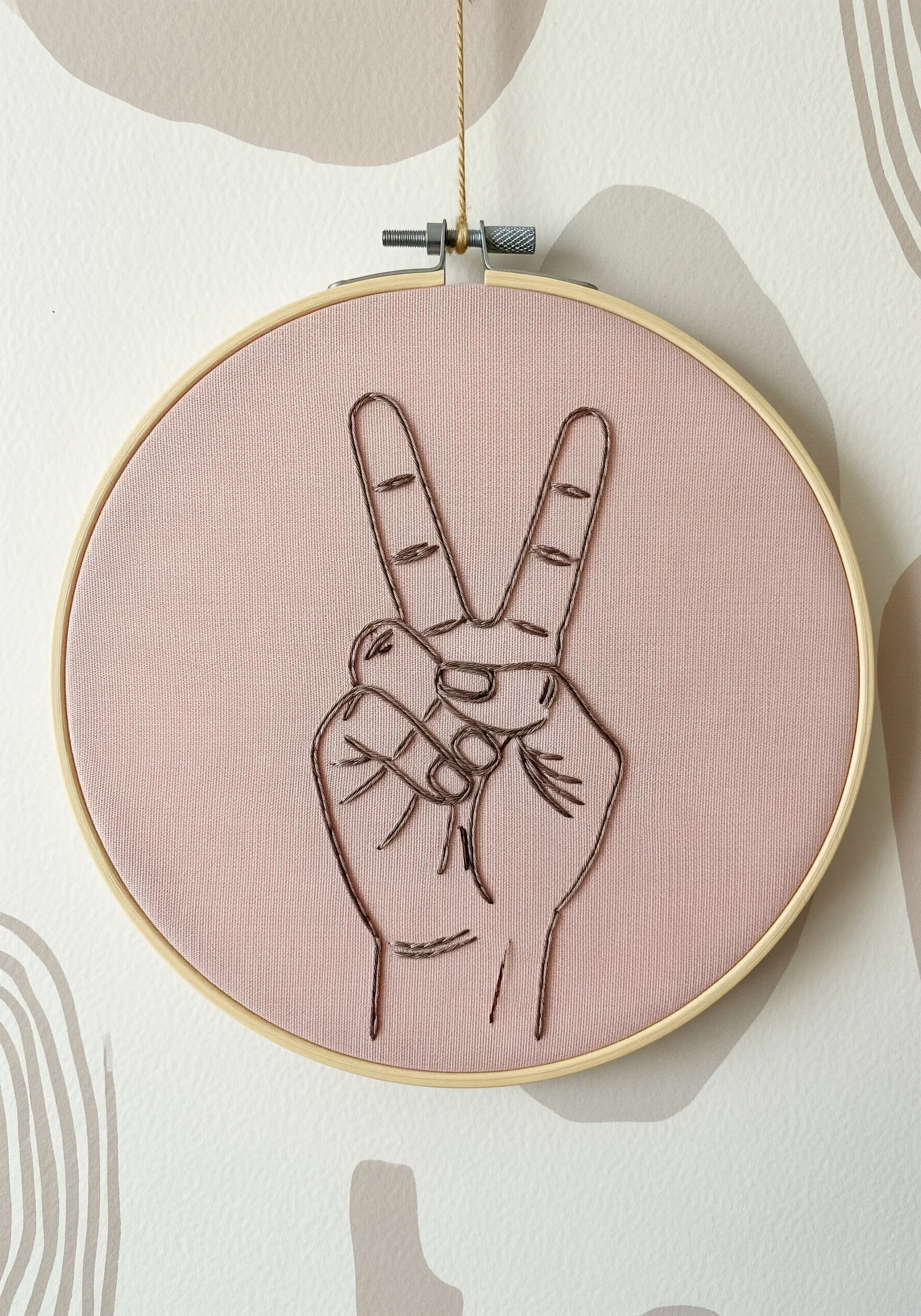 Peace sign hand embroidered with metallic thread on pink fabric.