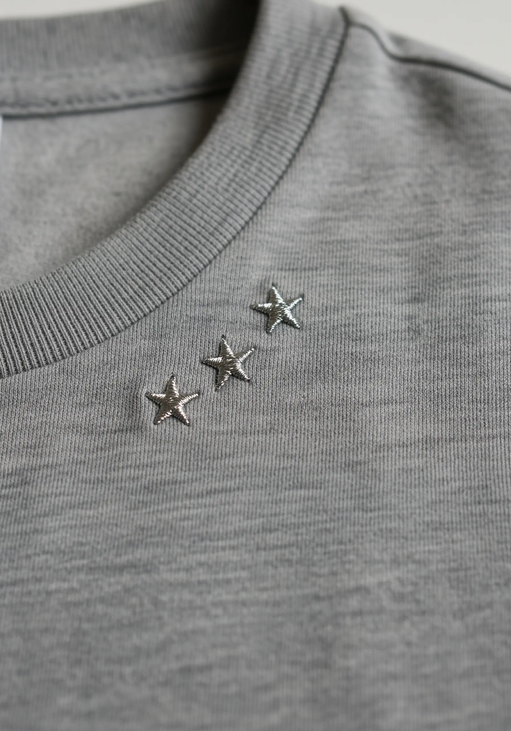 Three small, silver metallic stars embroidered on the collar of a grey t-shirt.
