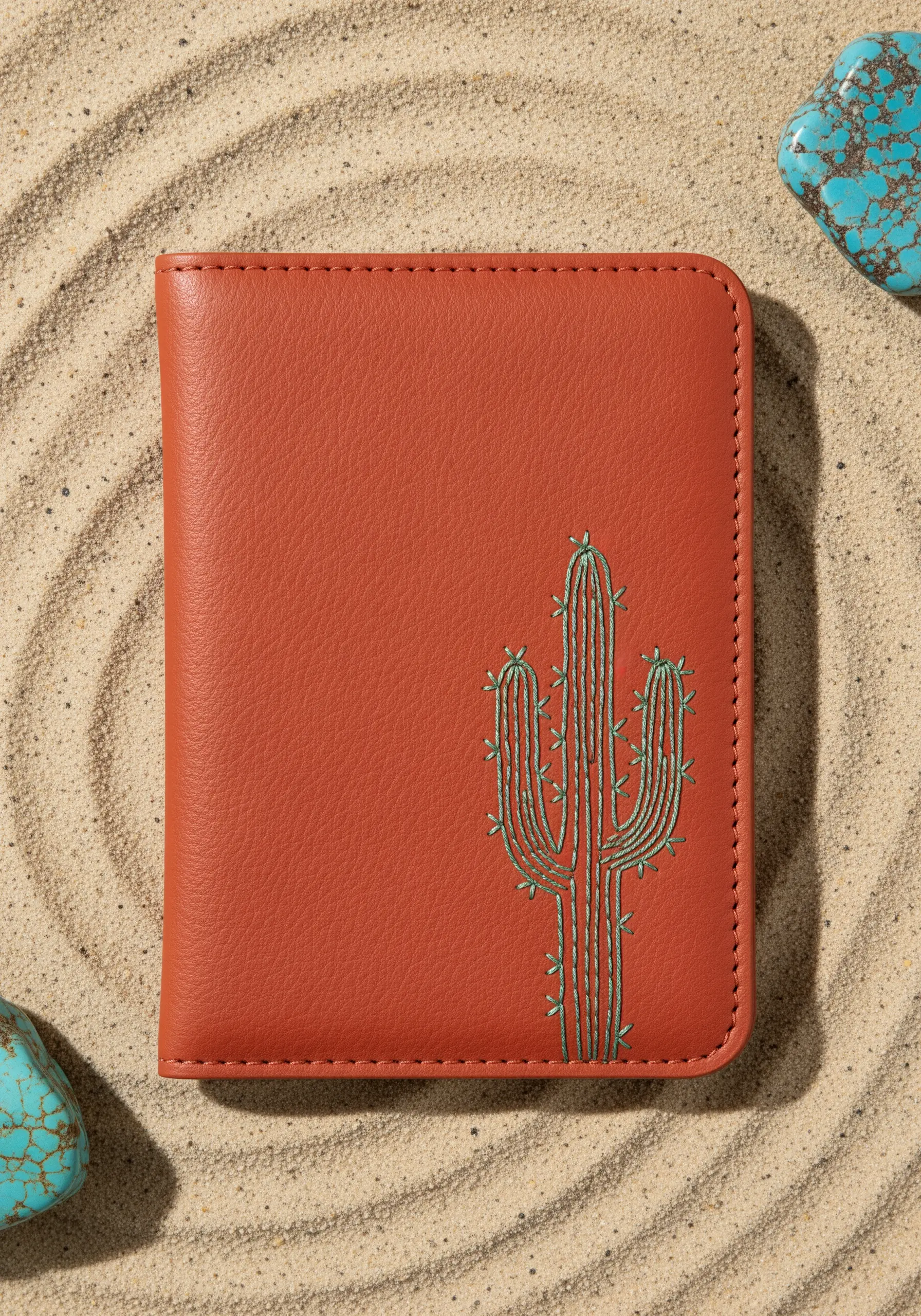 A saguaro cactus embroidered in green thread on a terracotta-colored leather passport cover.