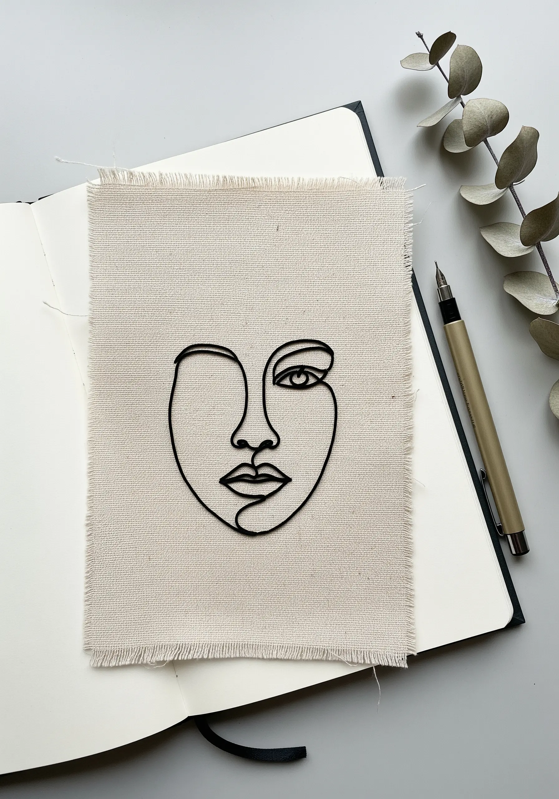 A single-line abstract face portrait embroidered in black thread on a neutral linen scrap.