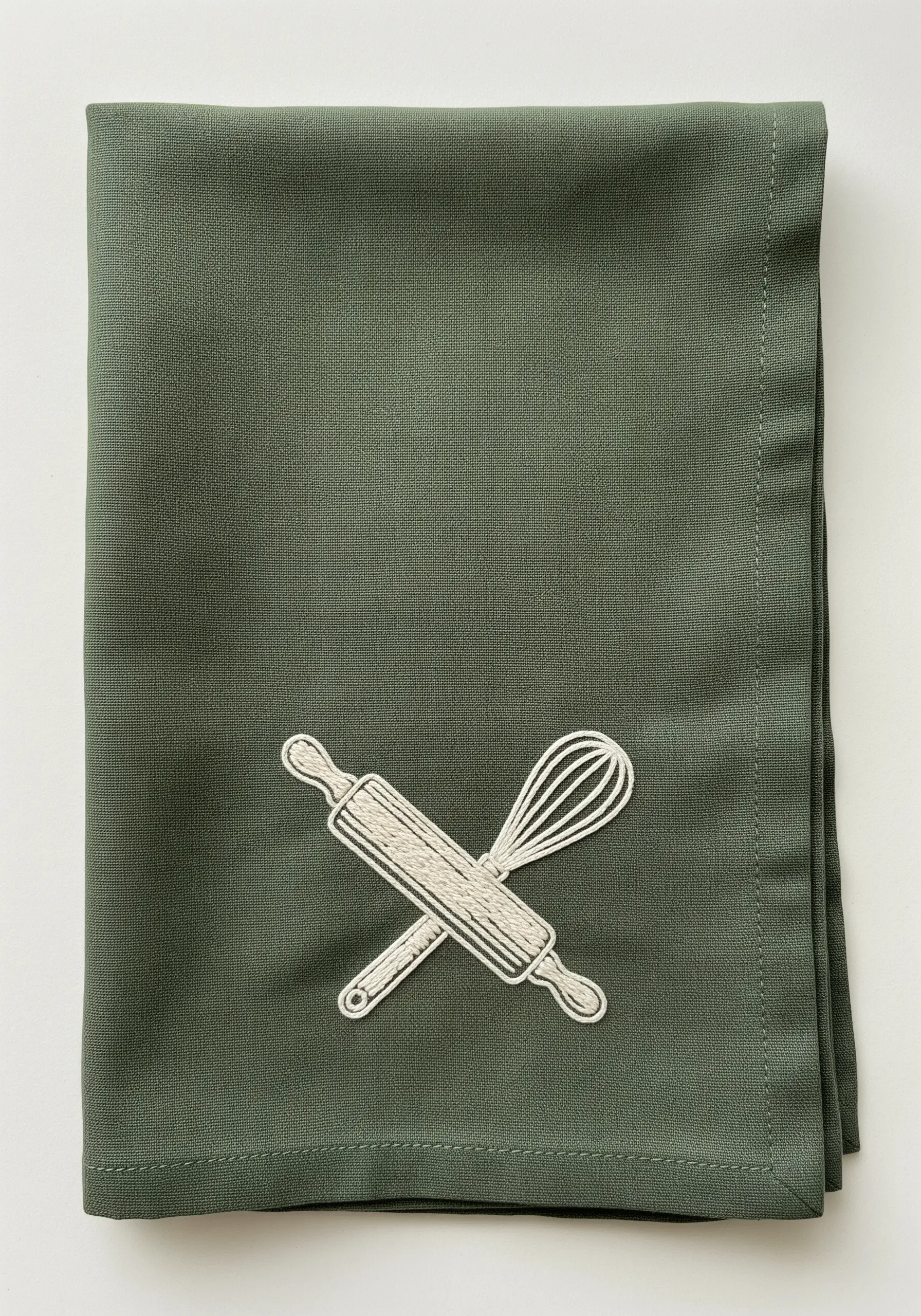 Minimalist white outline embroidery of a rolling pin and whisk on green fabric.