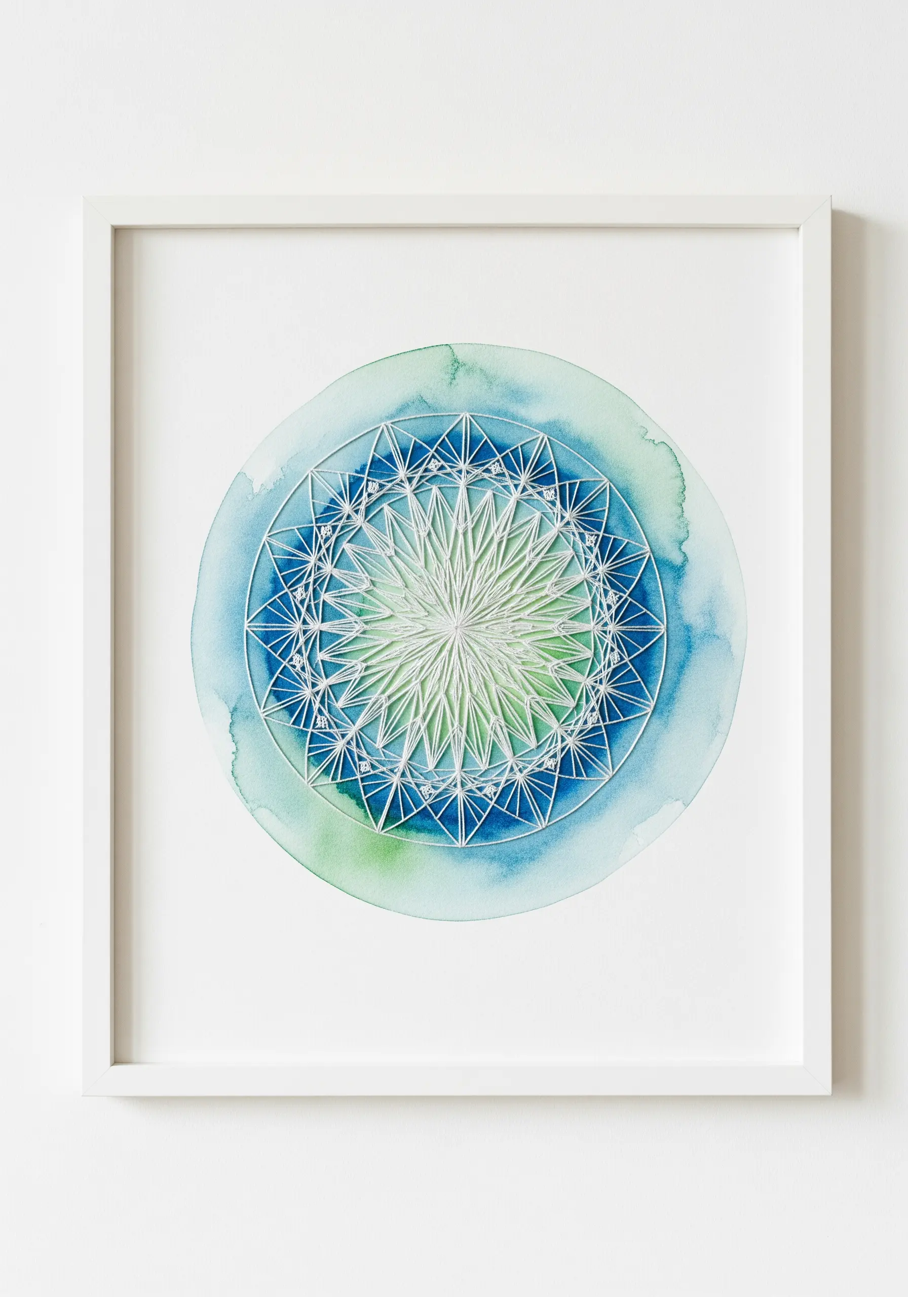 A geometric mandala stitched in white thread over a blue and green watercolor wash background.