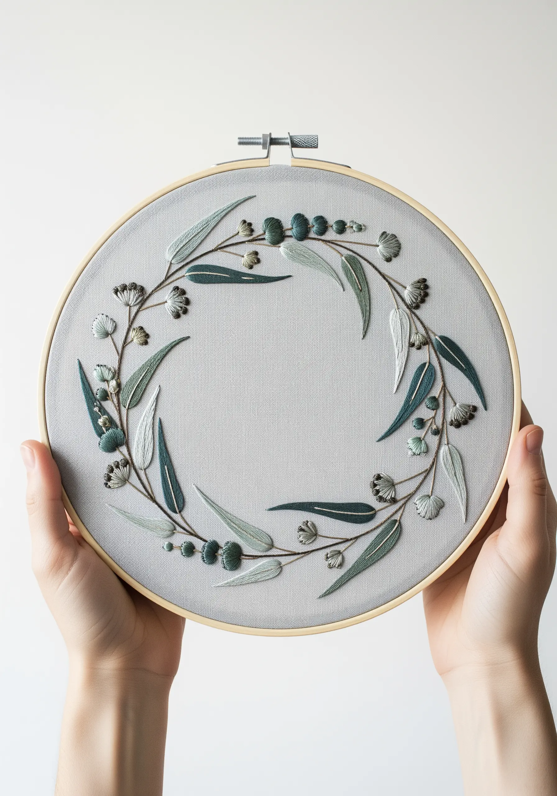 A delicate eucalyptus wreath embroidered in shades of dusty green on grey fabric.