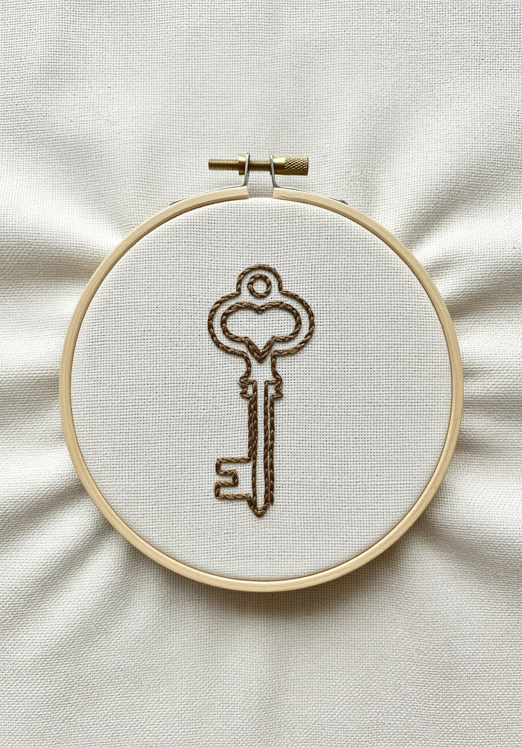 Outline of a vintage key embroidered using a brown chain stitch.