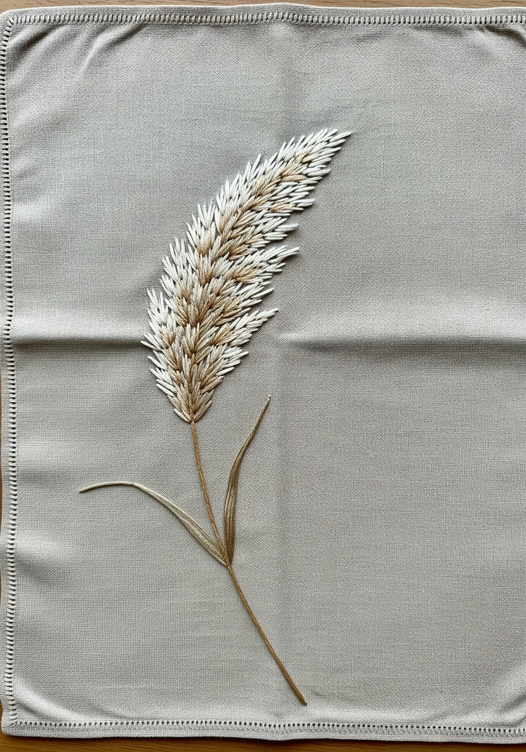 A realistic pampas grass frond embroidered on a grey napkin using thread painting techniques.