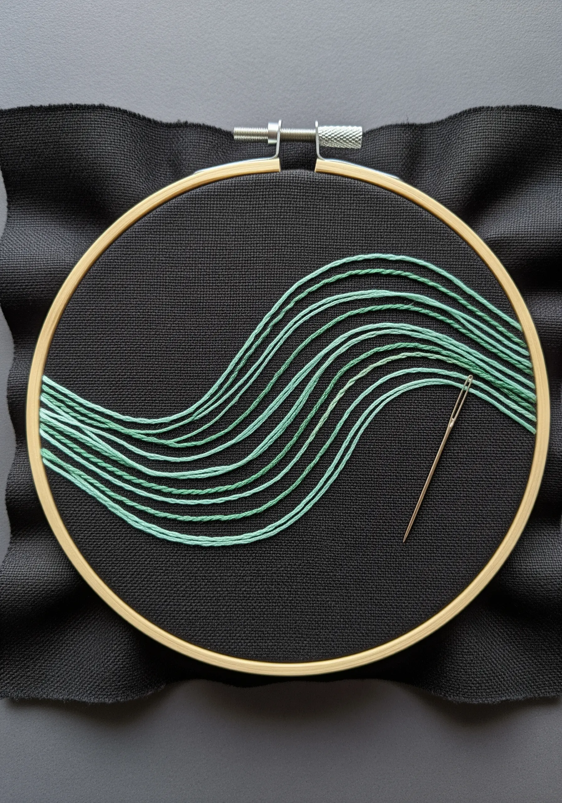 Abstract wavy lines in variegated green thread stretched across an embroidery hoop.