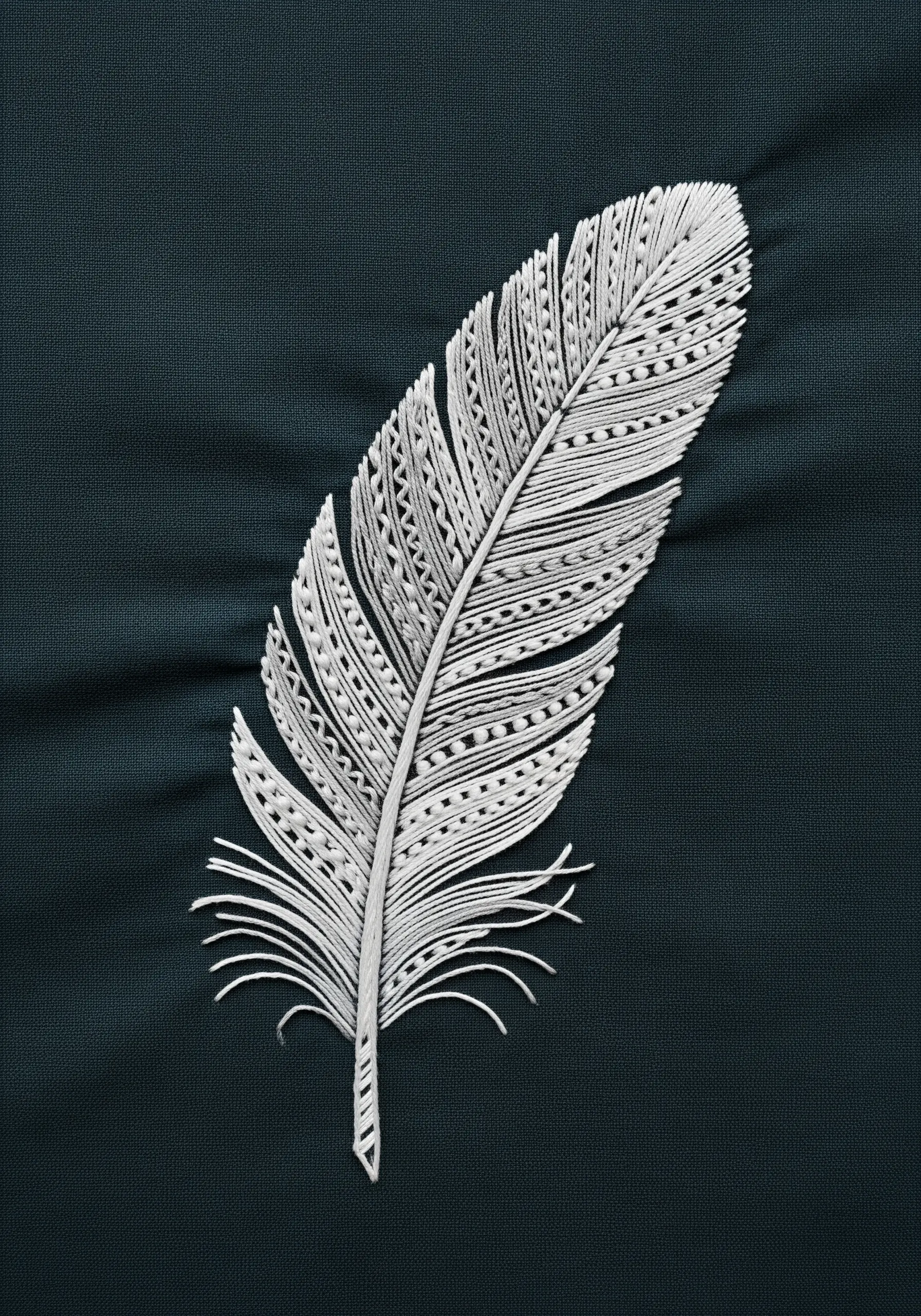 A highly detailed white feather embroidered with various stitch patterns on dark fabric.