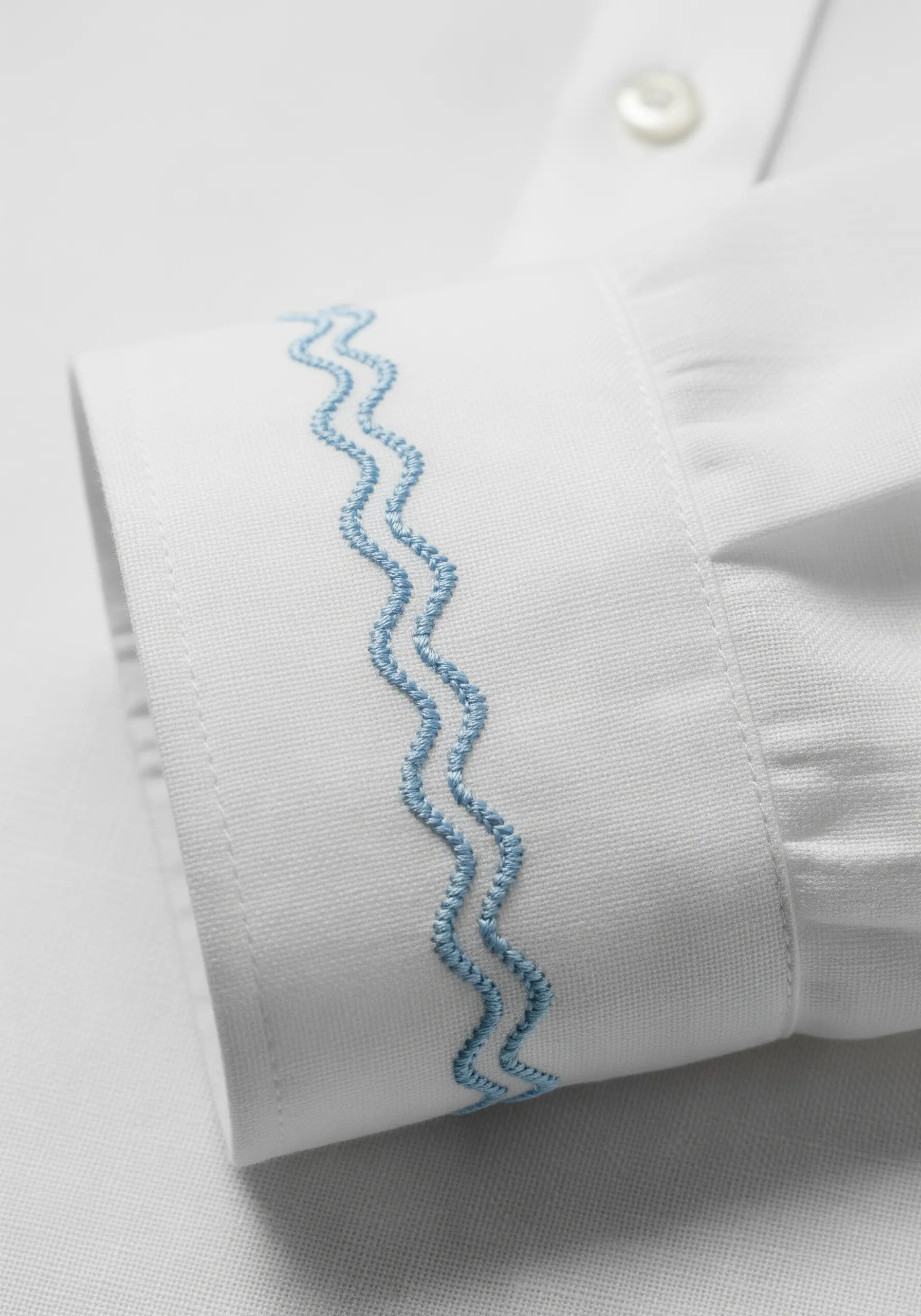 Two parallel wavy lines in blue chain stitch on a white shirt cuff.