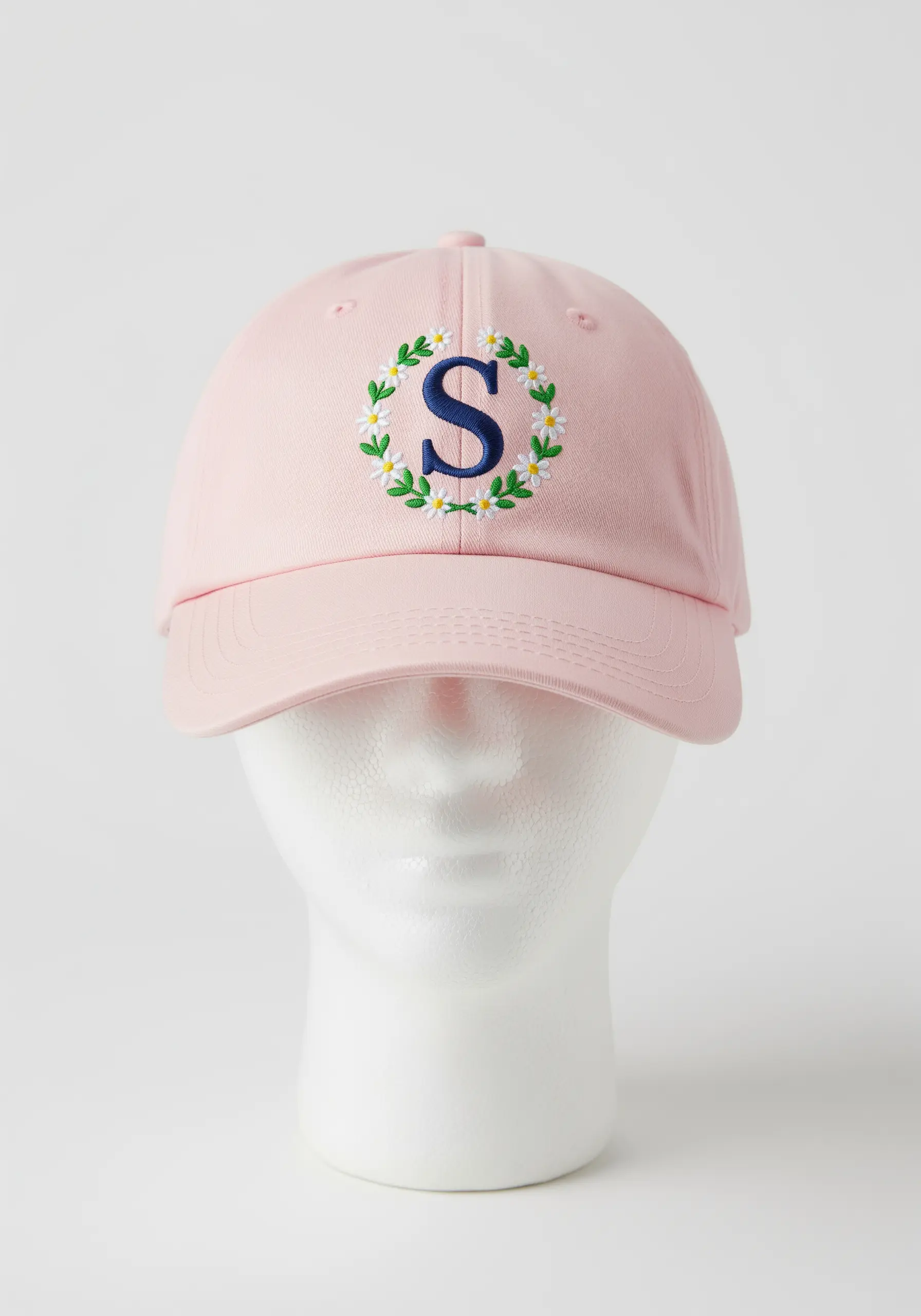 Navy blue 'S' initial with a white daisy wreath embroidered on a pink baseball cap.