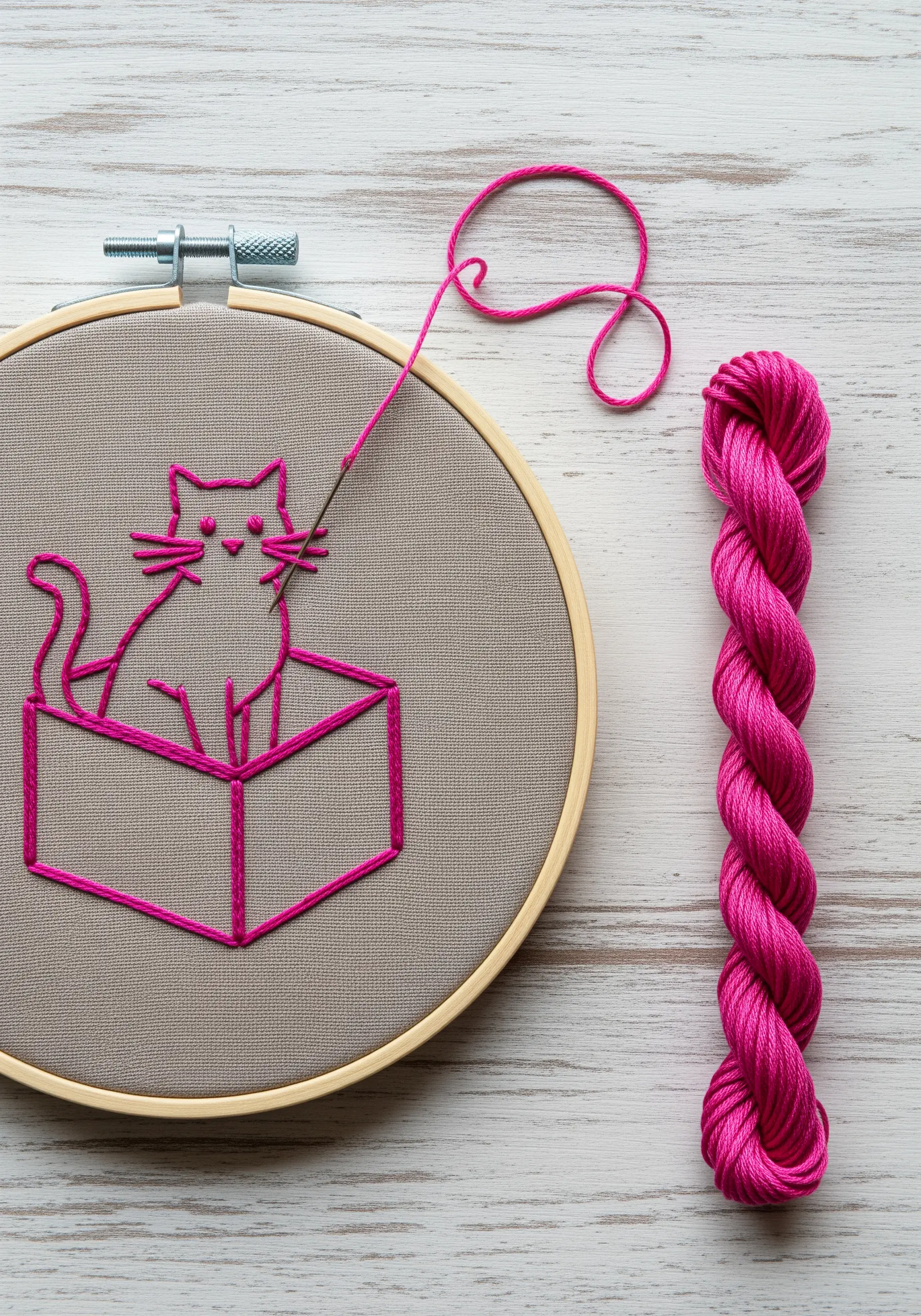 Vibrant pink line art embroidery of a cat sitting in a box on gray fabric.