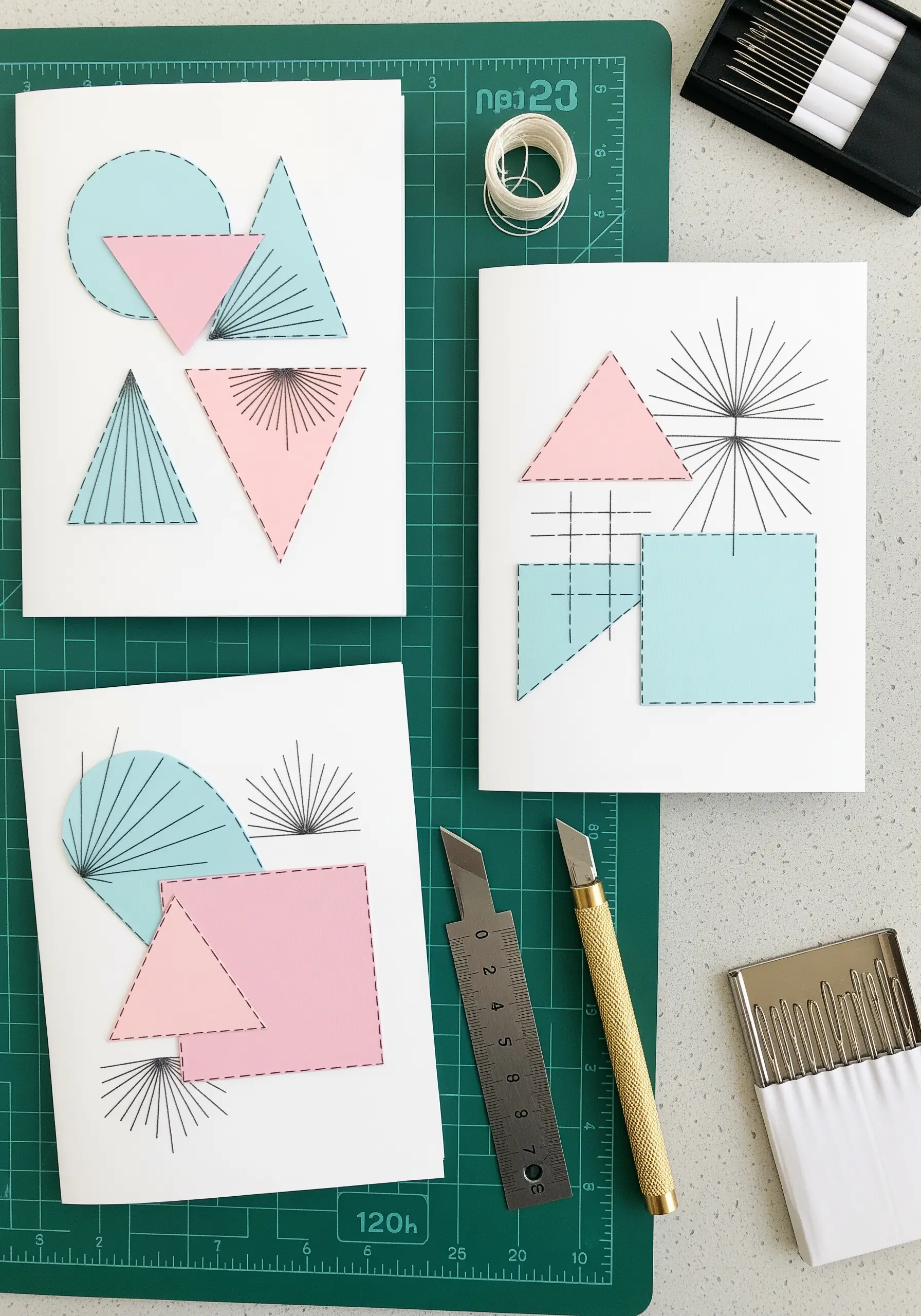 Geometric paper shapes on white cards embellished with radiating black straight stitches.