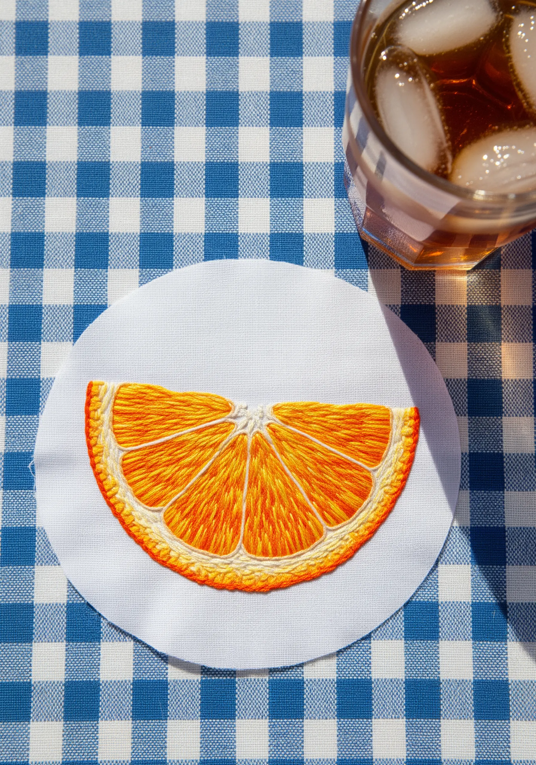 An embroidered orange slice on a white fabric circle, showing textured, directional satin stitch.