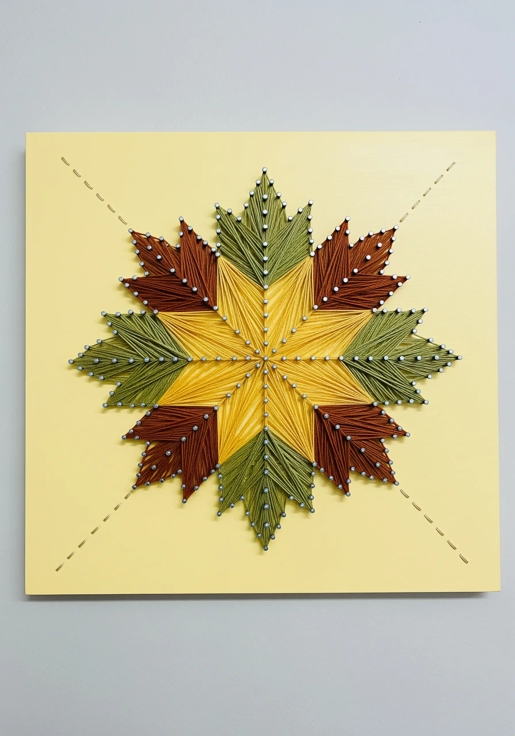 A string art barn quilt star with geometric sections in yellow, green, and brown thread.