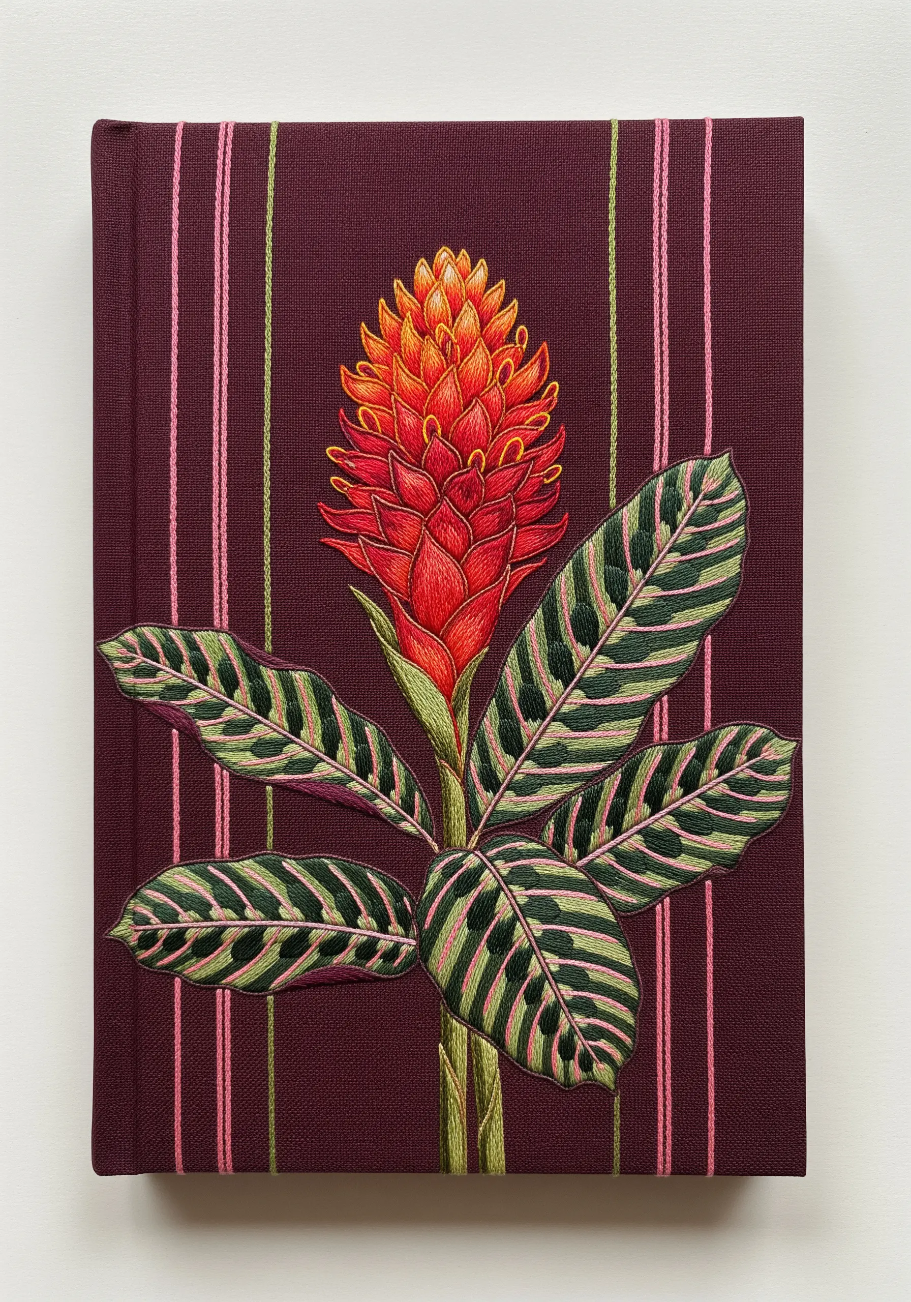 Elaborate embroidery of a ginger flower and patterned calathea leaves on a striped book cover.