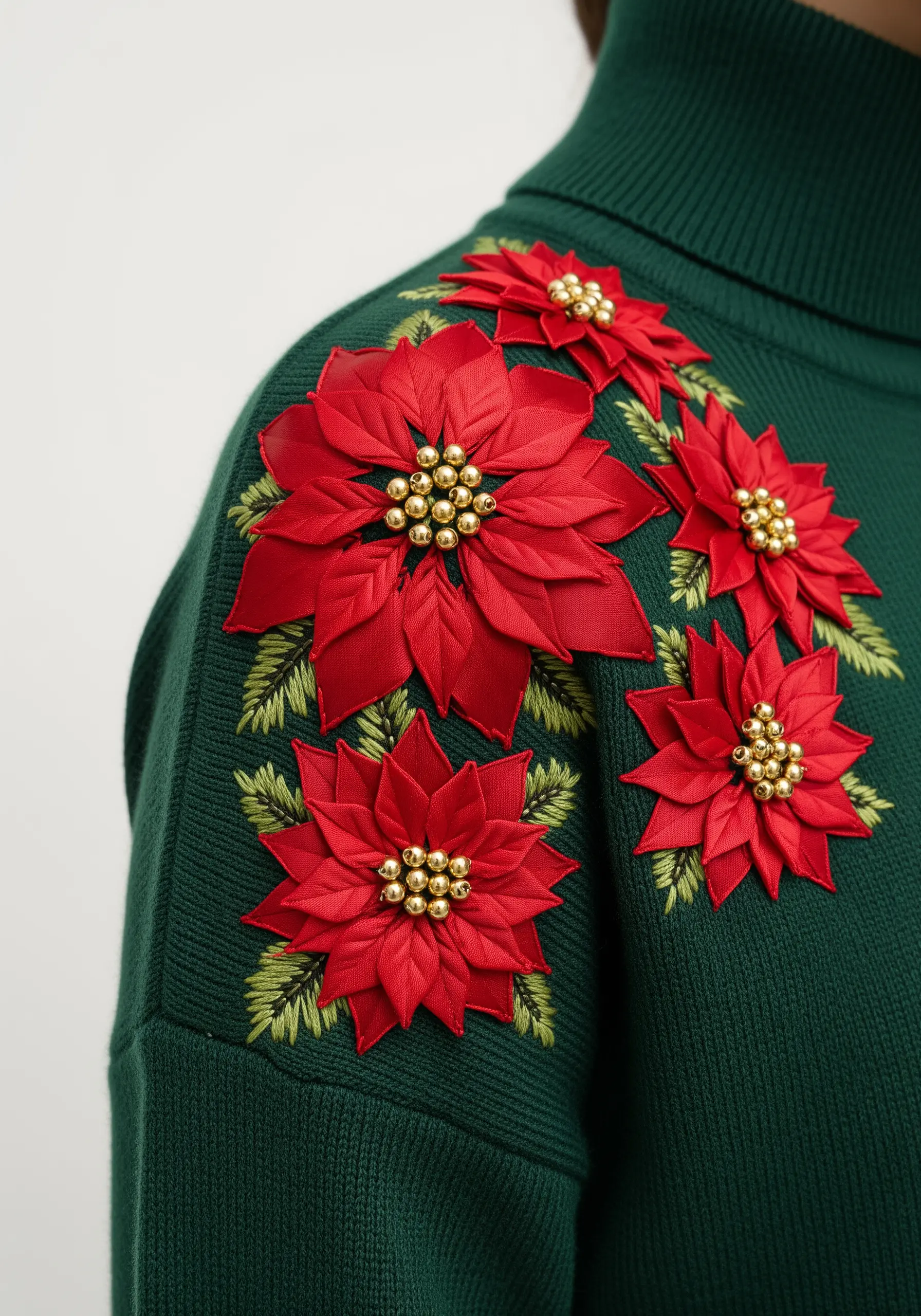 Dimensional red ribbon embroidery poinsettias with beaded centers on a green sweater.
