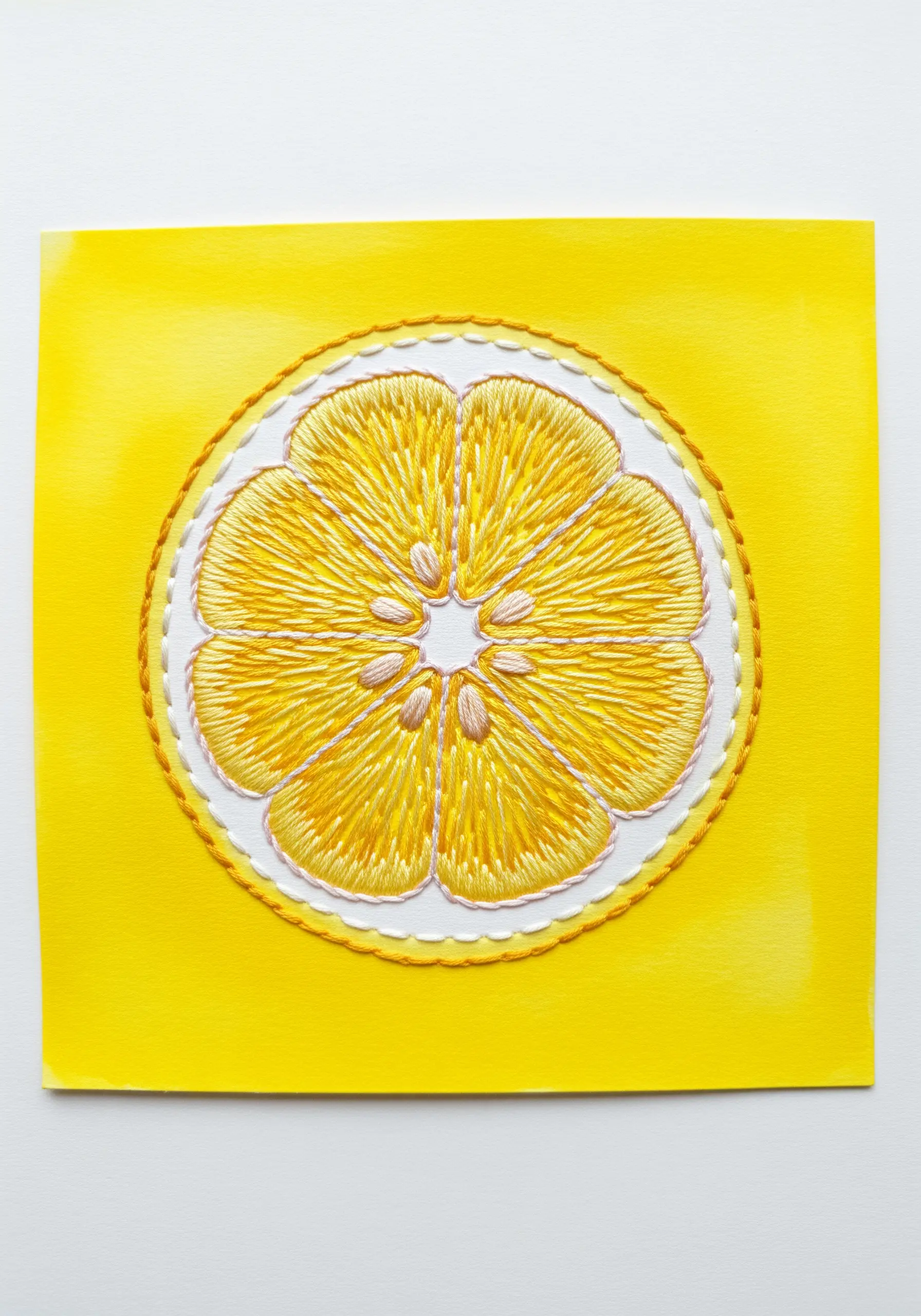 A lemon slice filled with yellow satin stitch on a yellow watercolor background