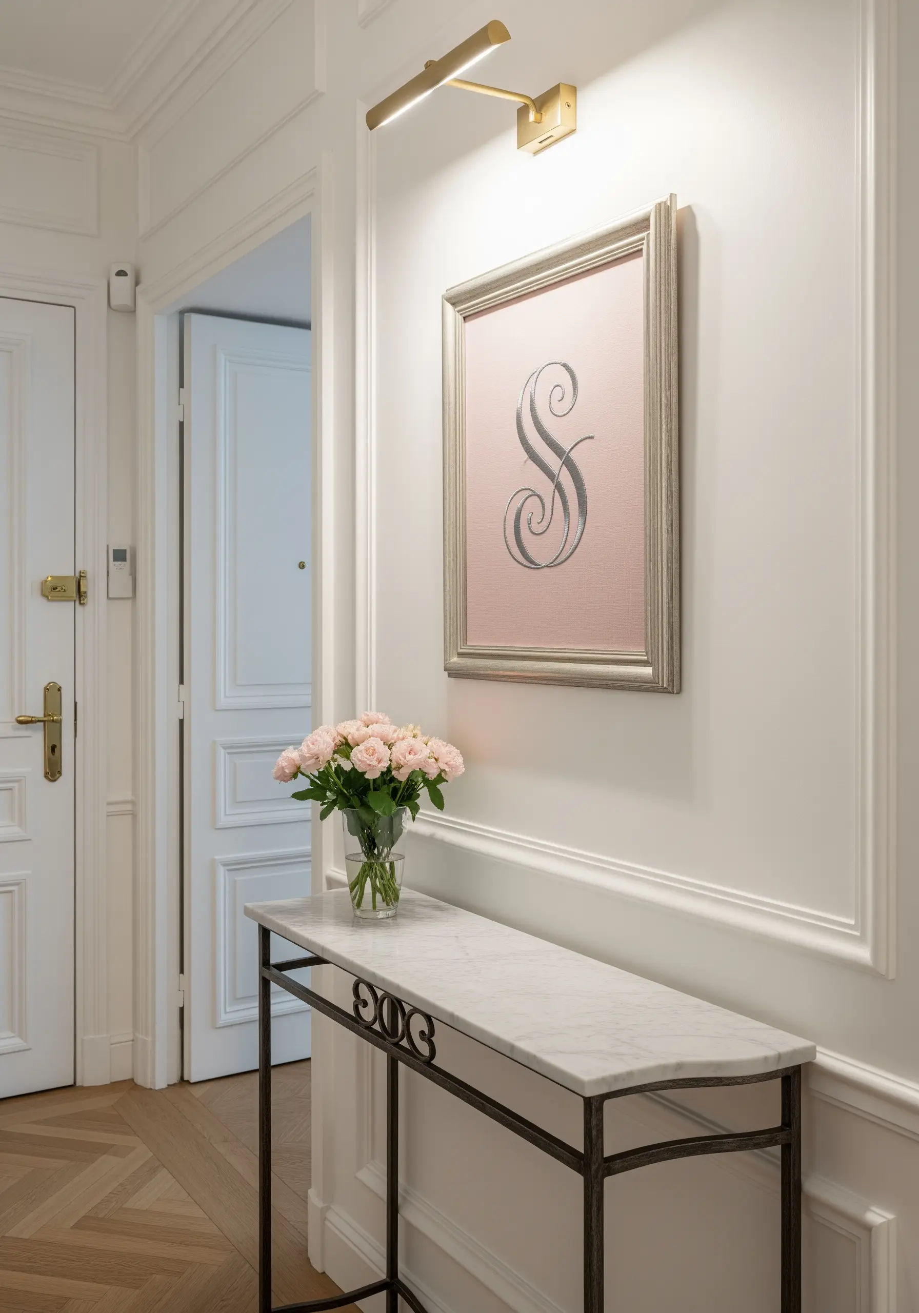 A large, framed monogram with a delicate grey script 'S' on pale pink fabric.
