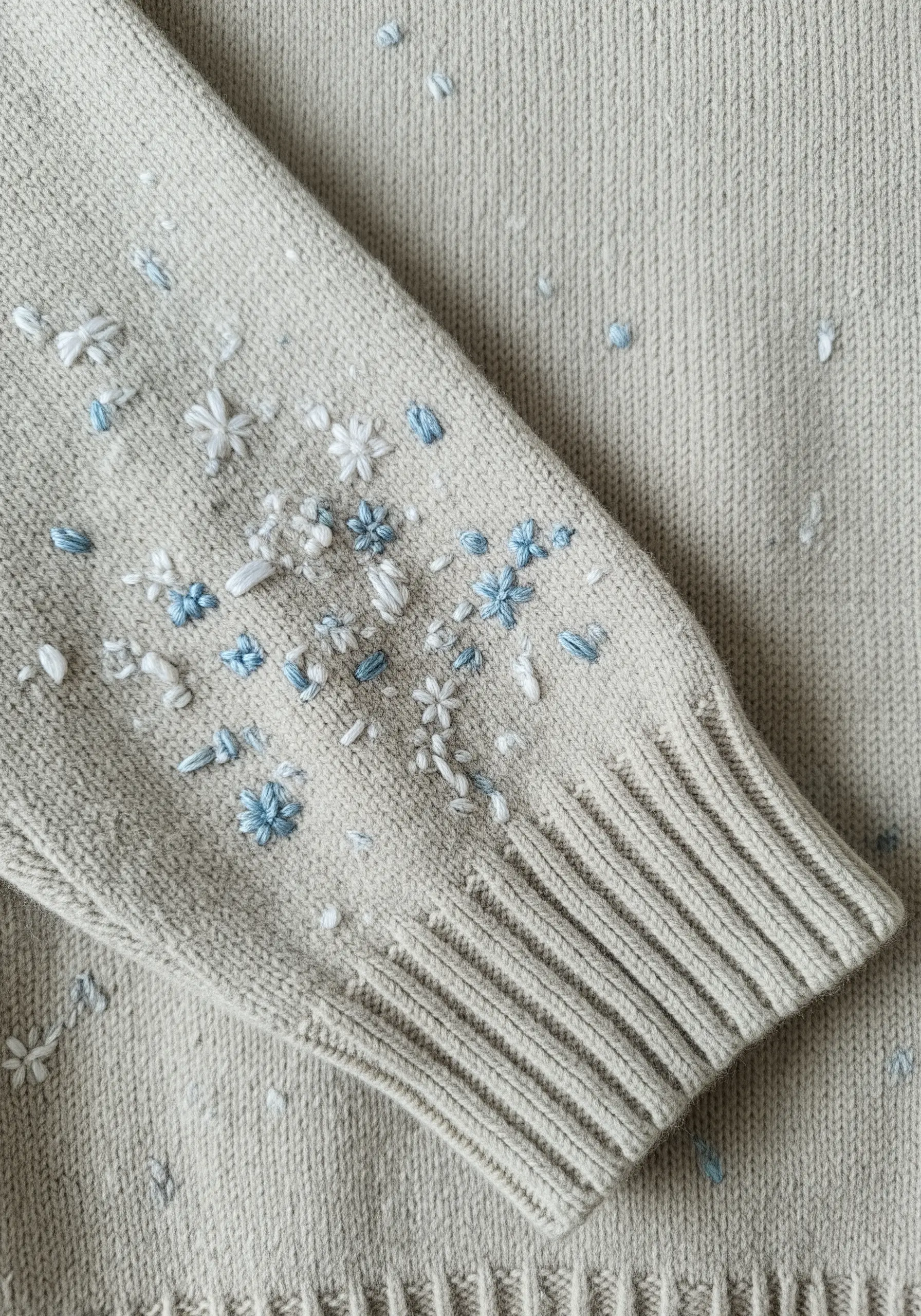 Scattered blue and white textural embroidery stitches on the cuff of a knit sweater.