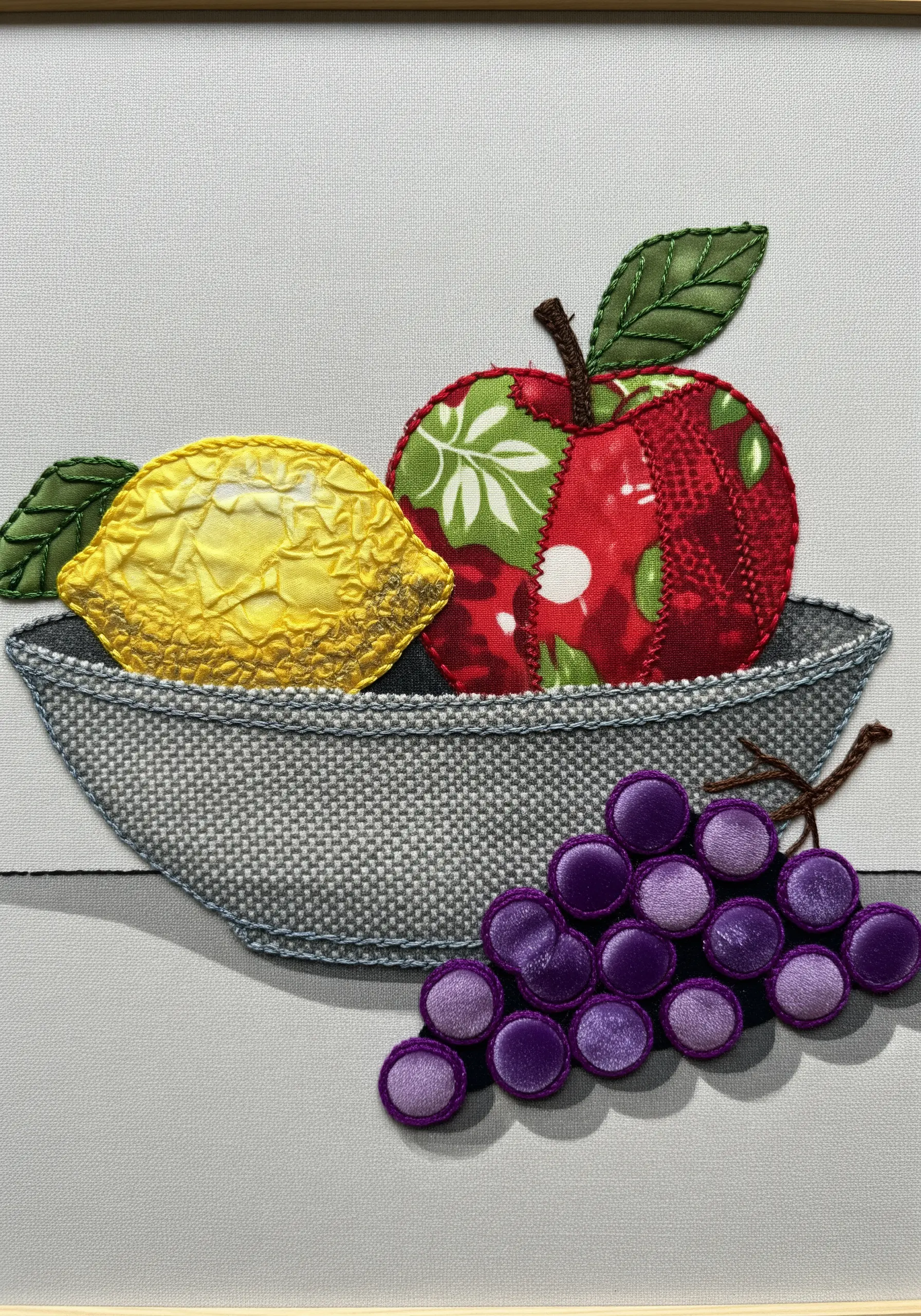 Appliqué still life of a fruit bowl with 3D padded grapes and textured lemon.