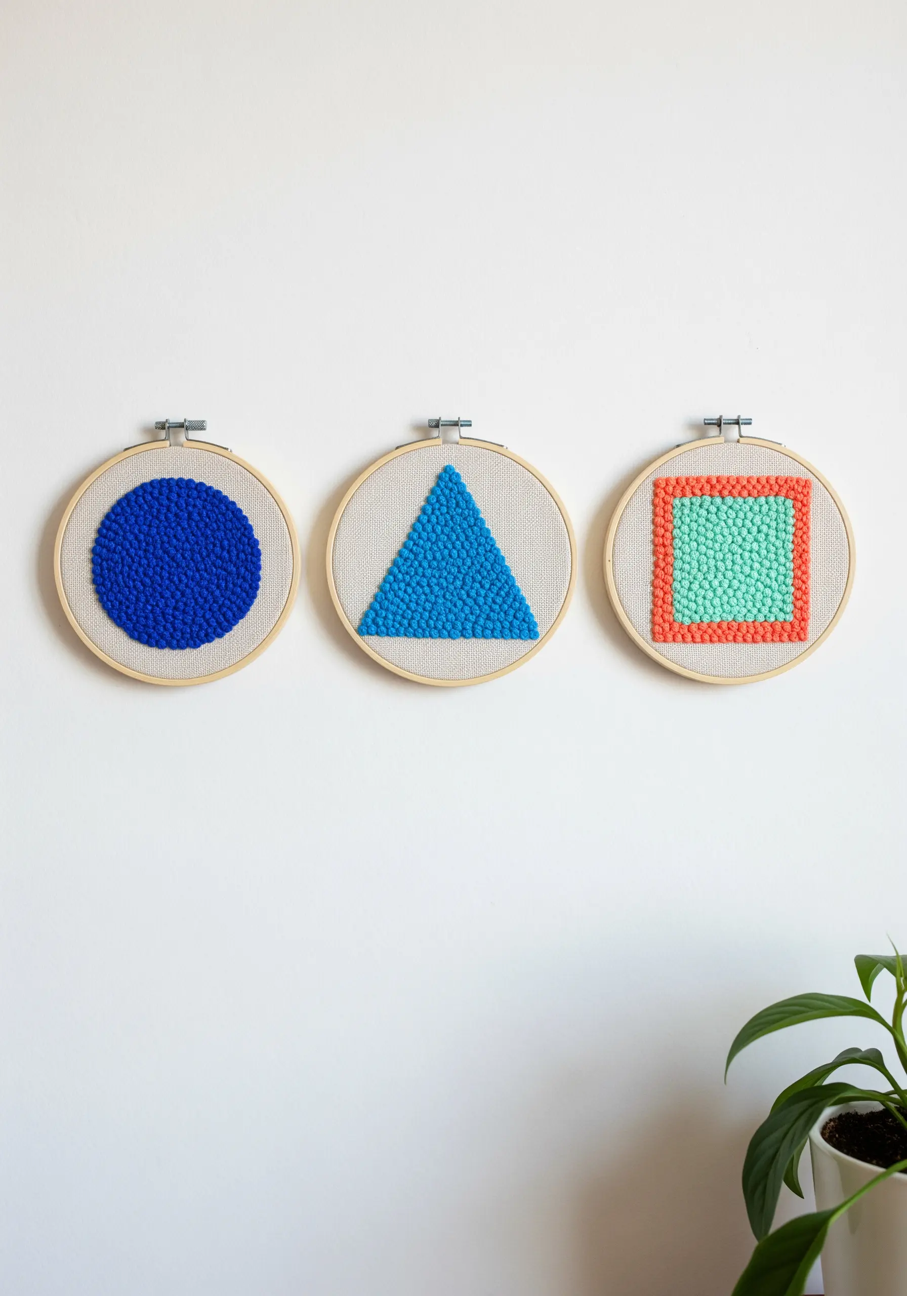Three embroidery hoops with geometric shapes in punch needle texture.