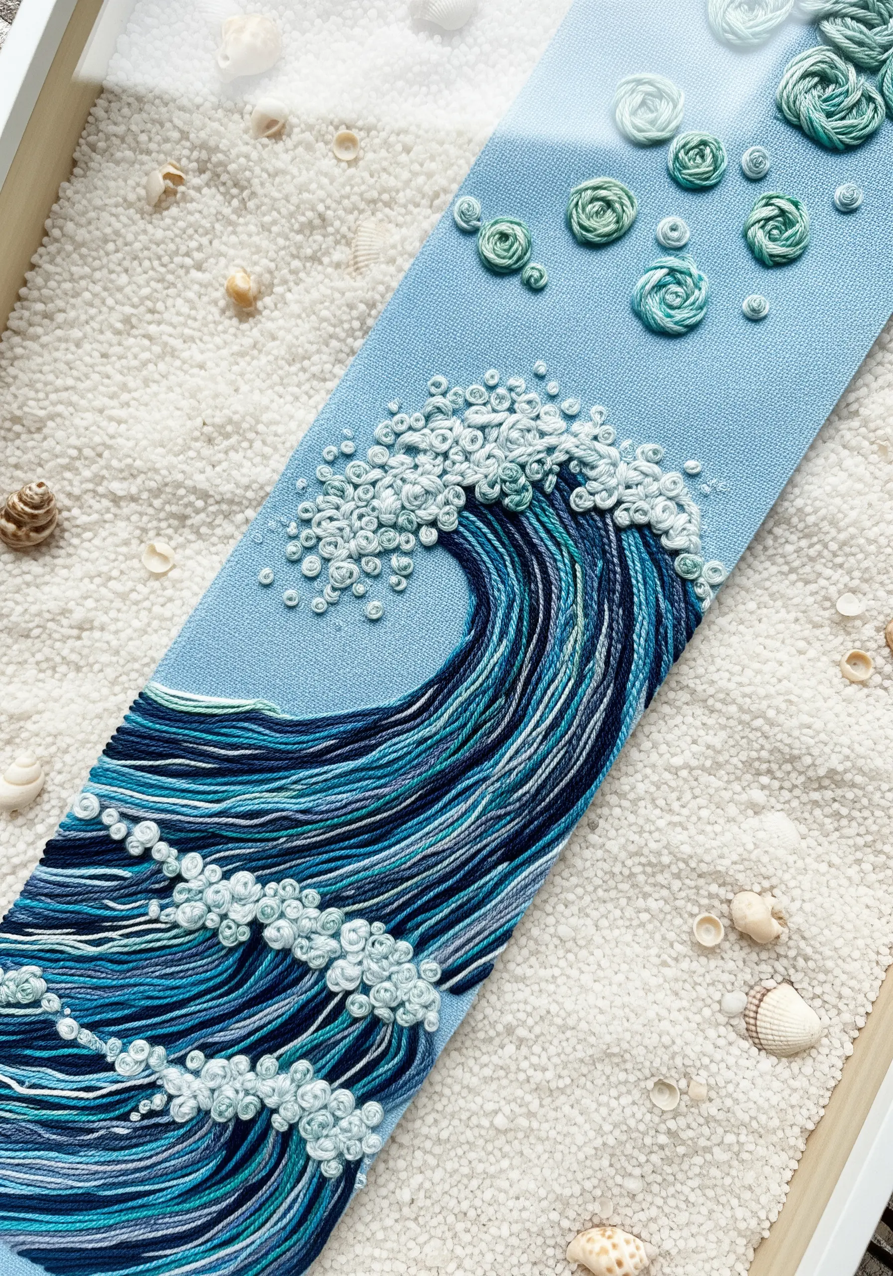 An embroidered ocean wave with French knot seafoam and layered straight stitches in shades of blue.