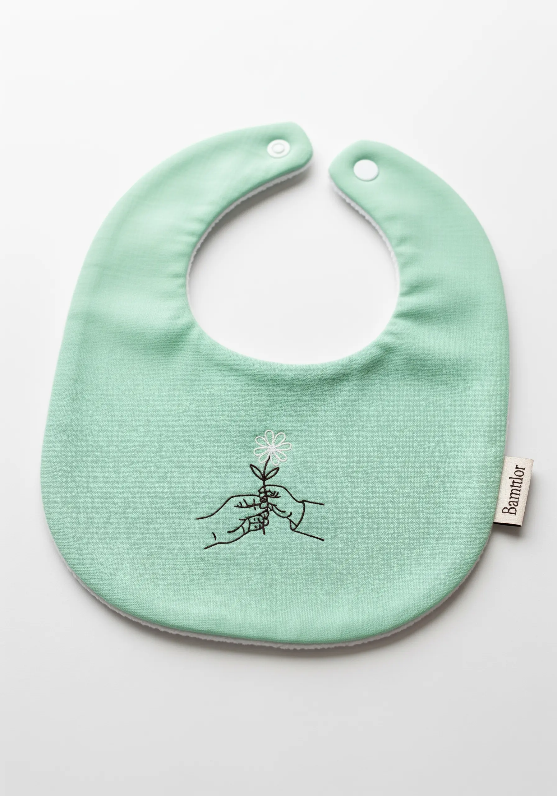 A minimalist design of two hands holding a flower, embroidered on a mint green baby bib.