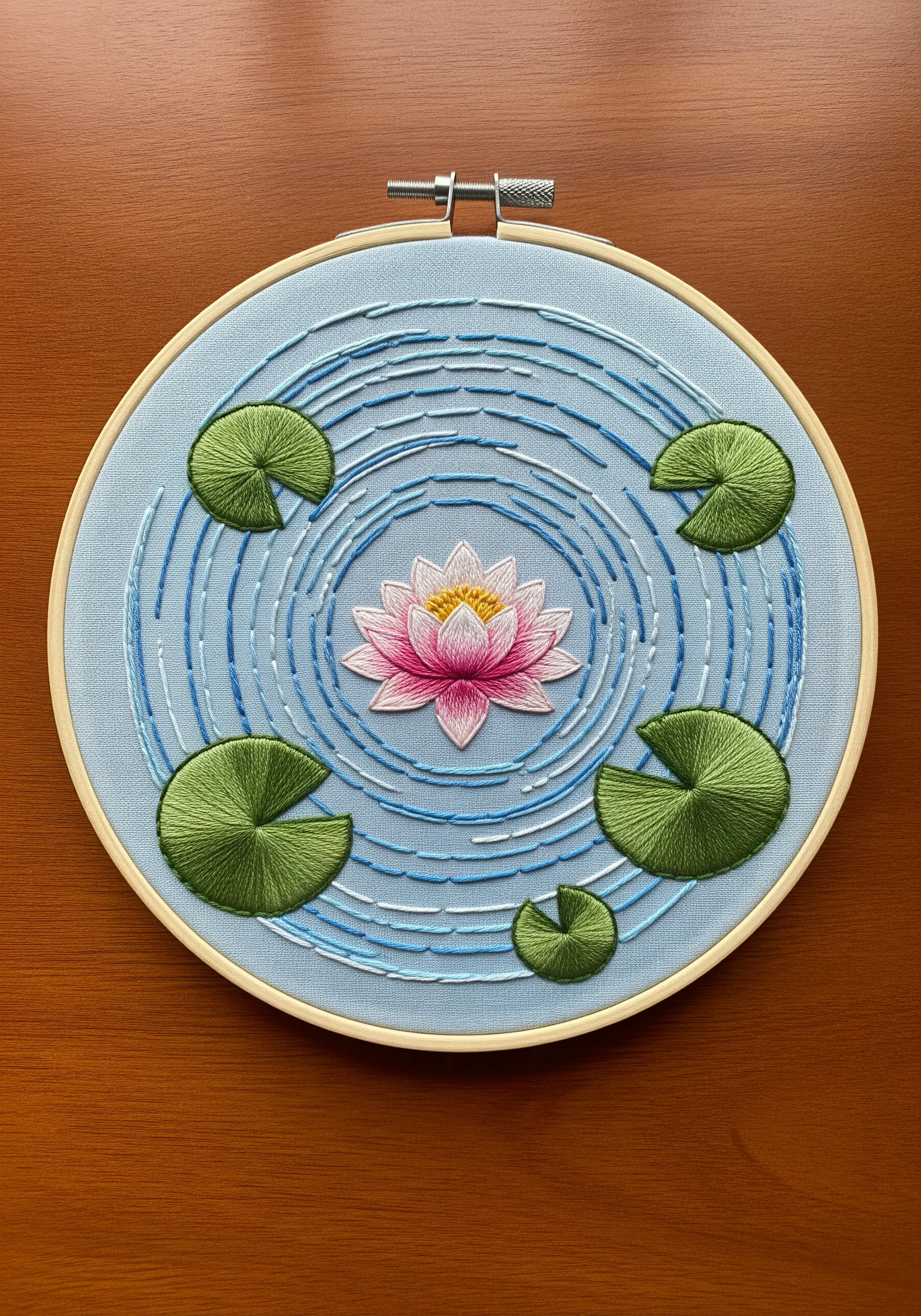 Embroidered water lily and pads on a blue background with stitched water ripples.