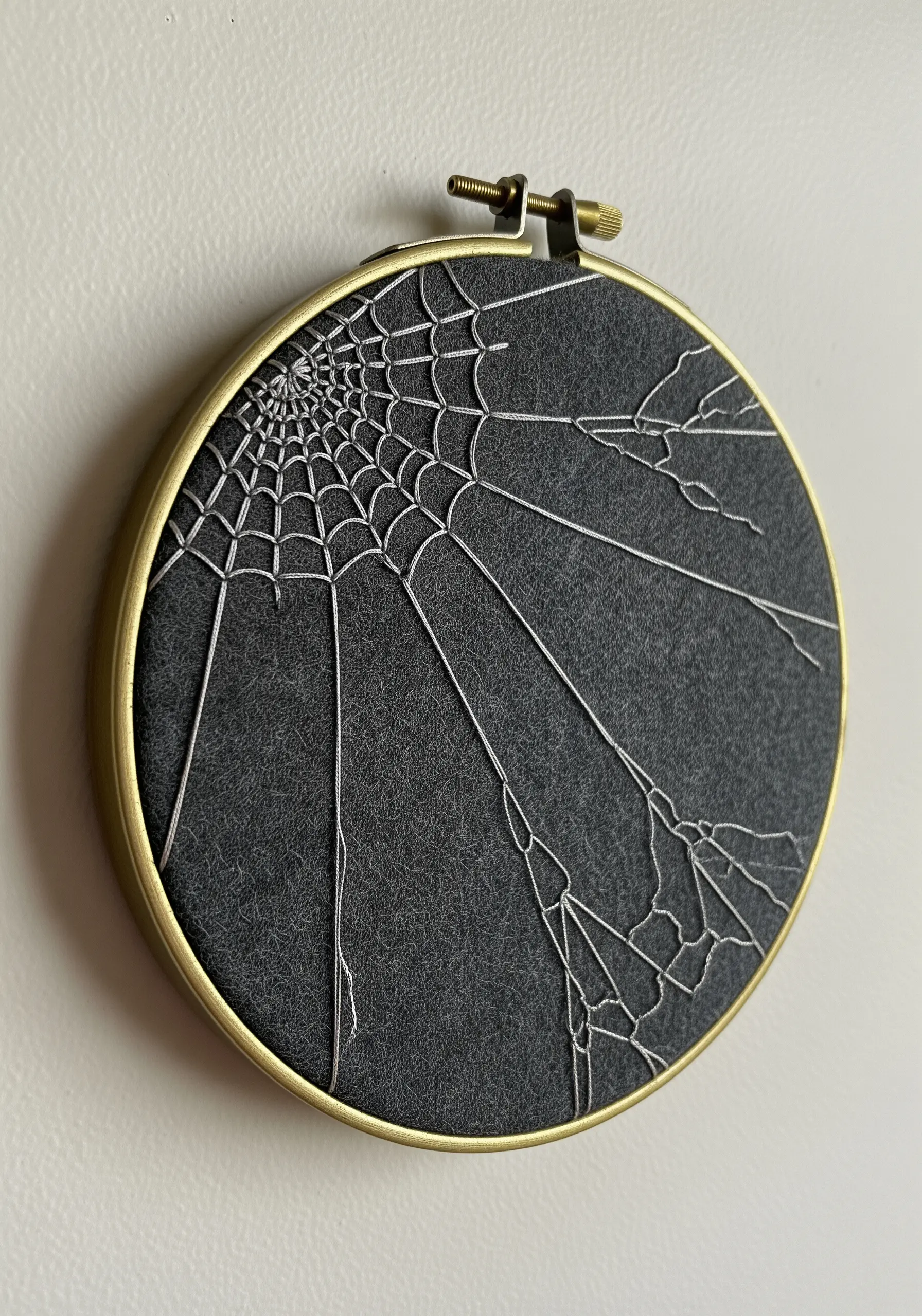 A delicate, realistic spiderweb embroidered in silver thread on dark grey fabric.