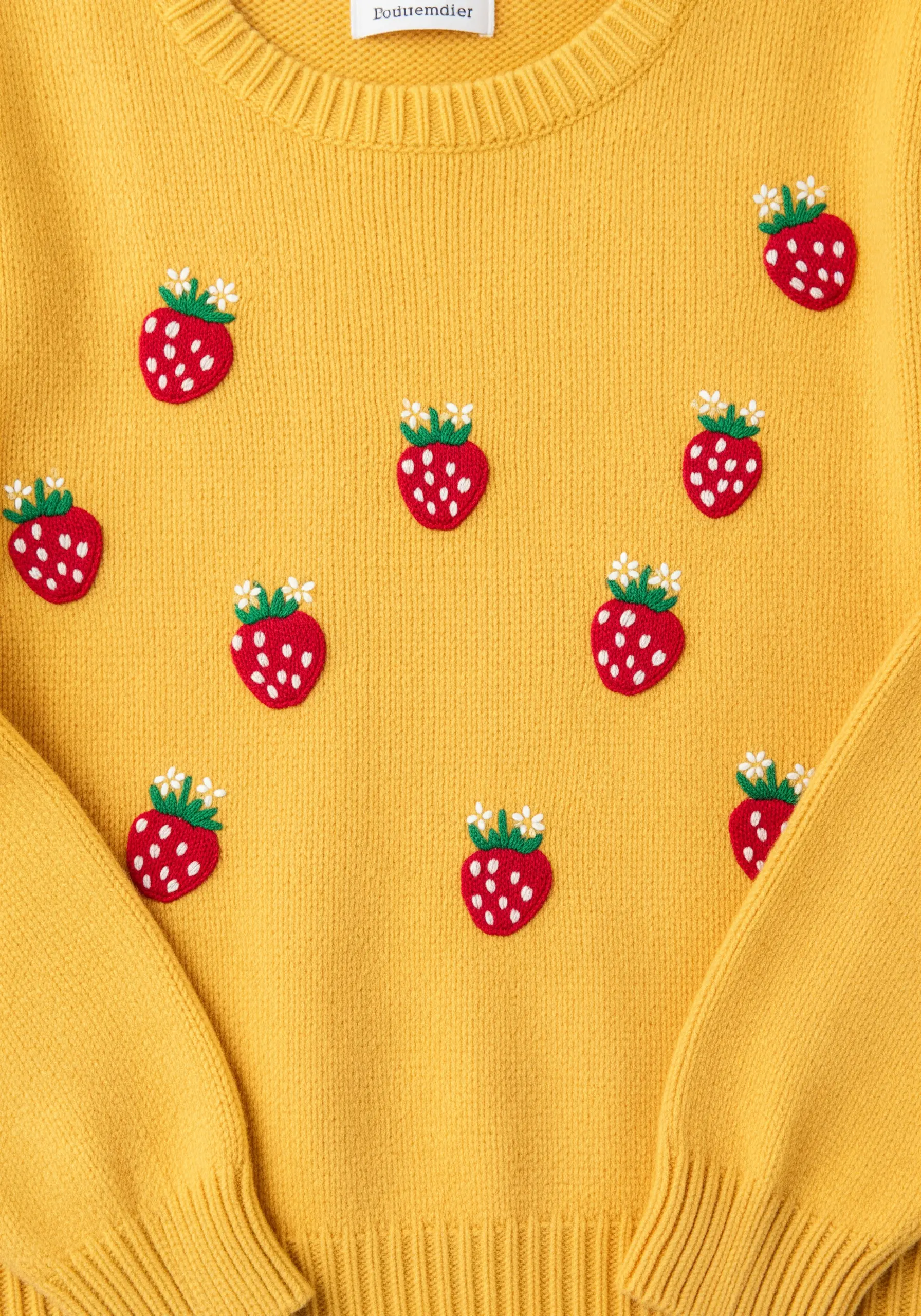 A scattered pattern of small, embroidered red strawberries on a bright yellow sweater.