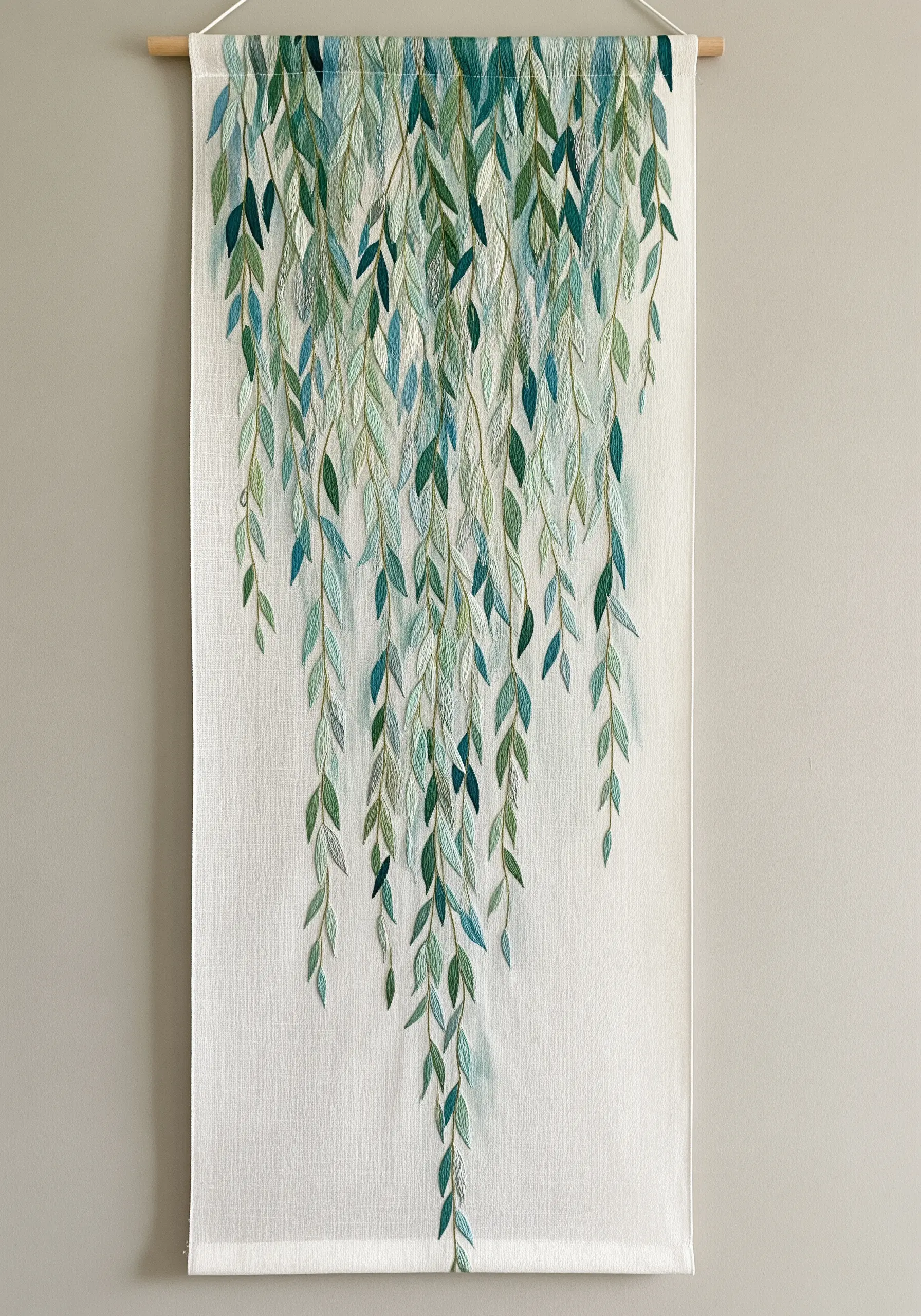 Wall hanging with embroidered weeping willow leaves in shades of green and blue cascading down.