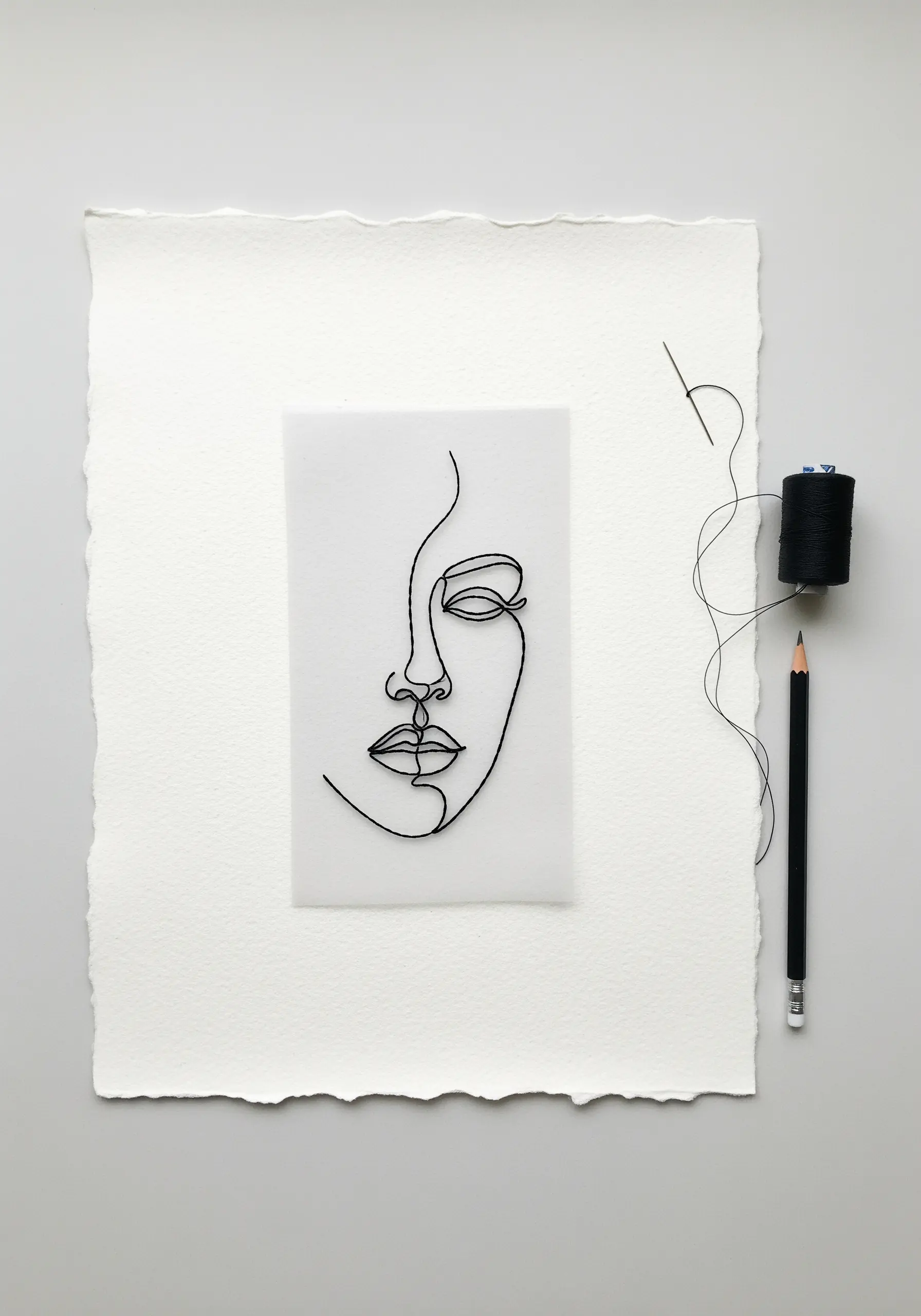 A minimal, single-line face embroidered with black thread directly onto a sheet of translucent vellum.