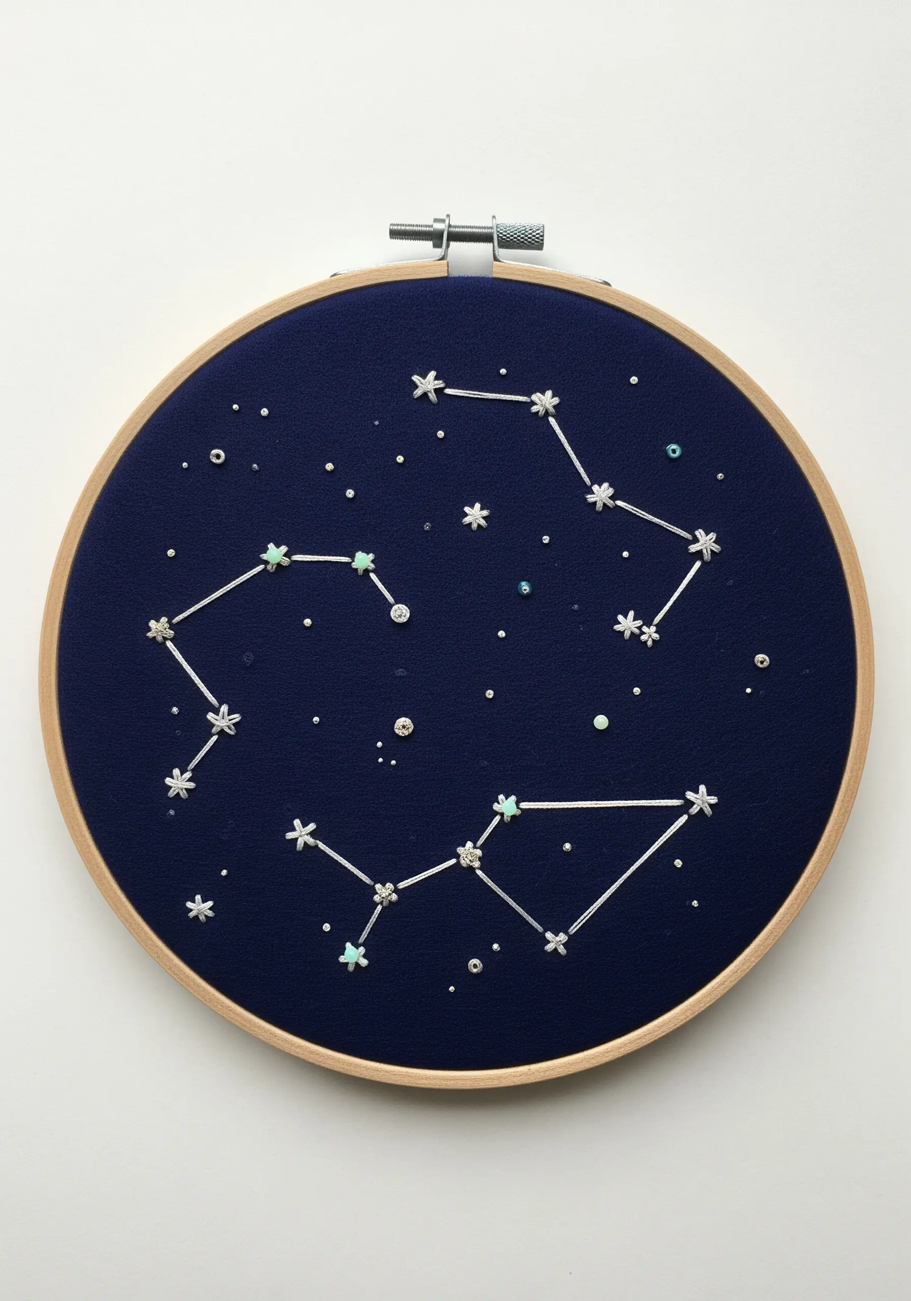 Minimalist embroidery hoop of constellations on dark blue fabric using beads and white thread.