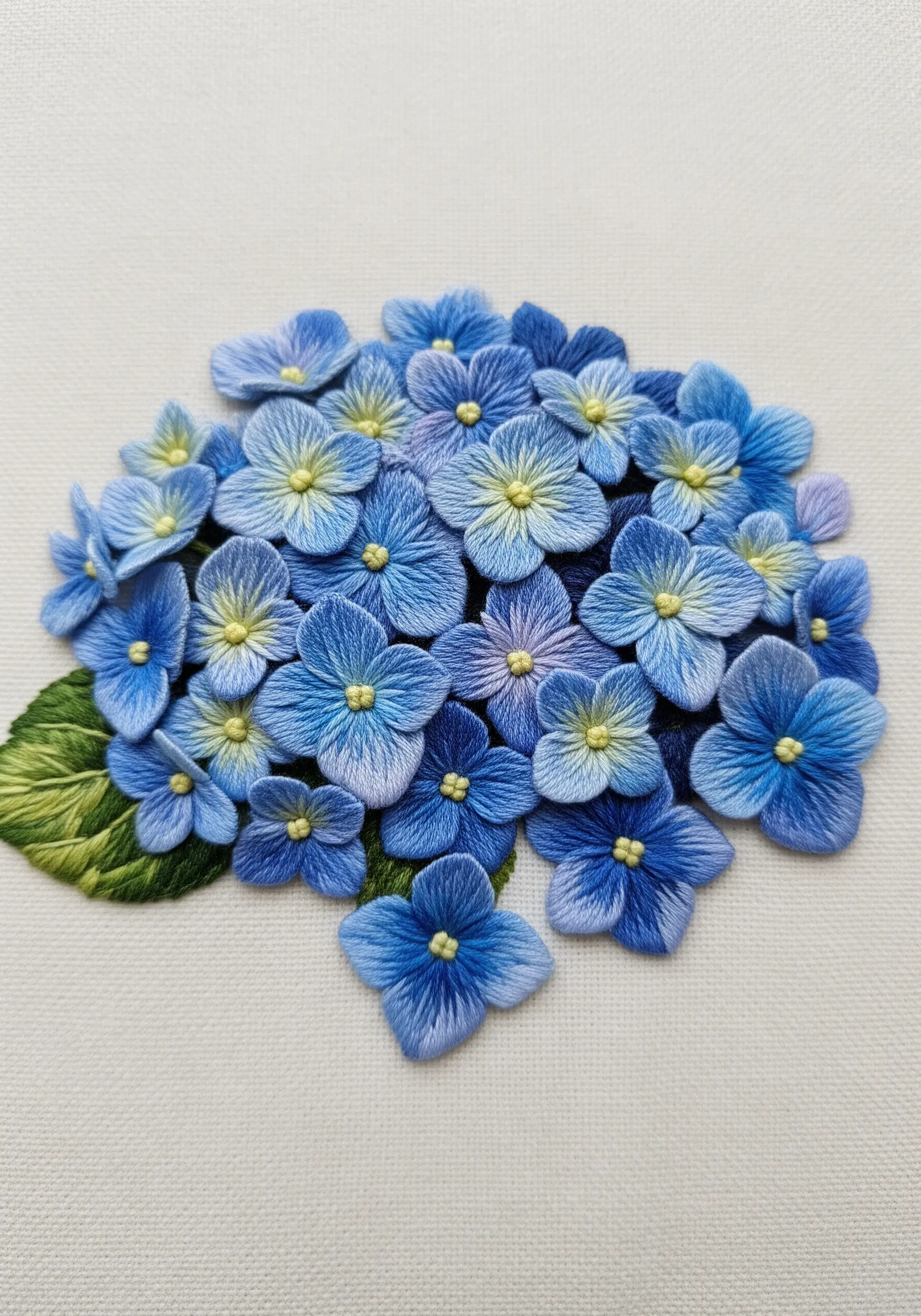A cluster of blue and purple thread-painted hydrangea flowers on white fabric.