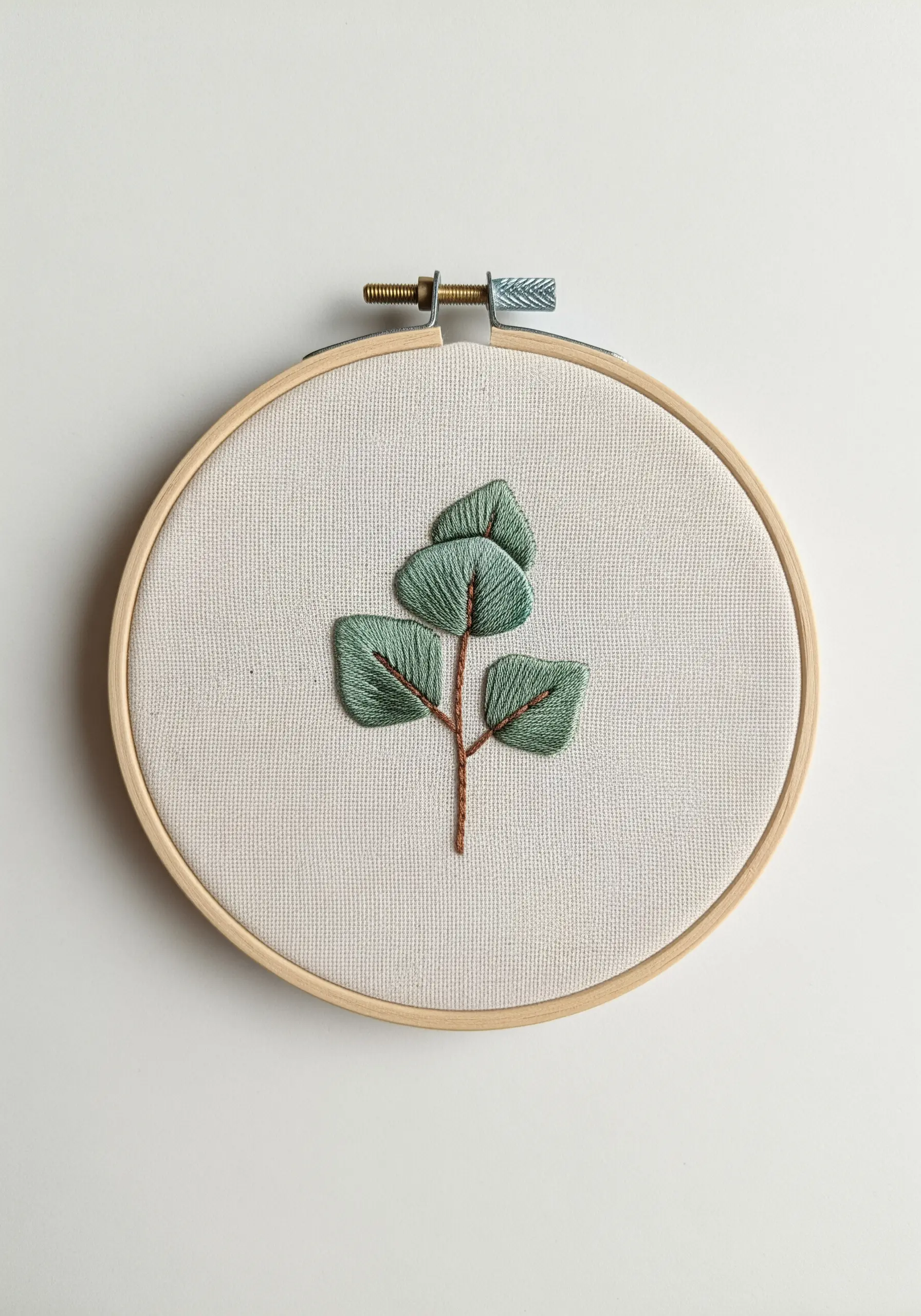 Stylized eucalyptus branch with satin-stitched leaves on a thin brown stem.