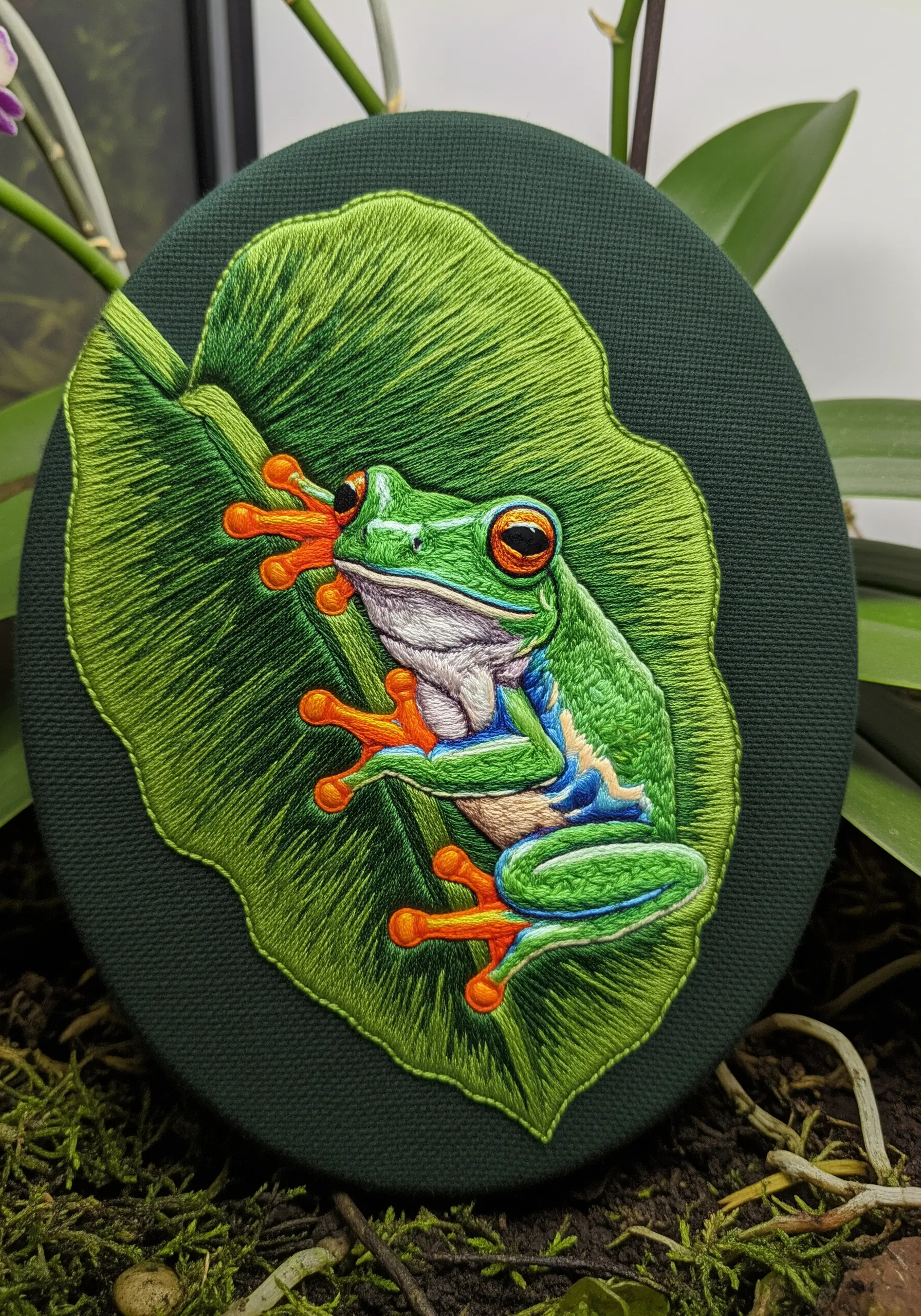 A vibrant green tree frog embroidered with smooth satin stitches to mimic slick skin.