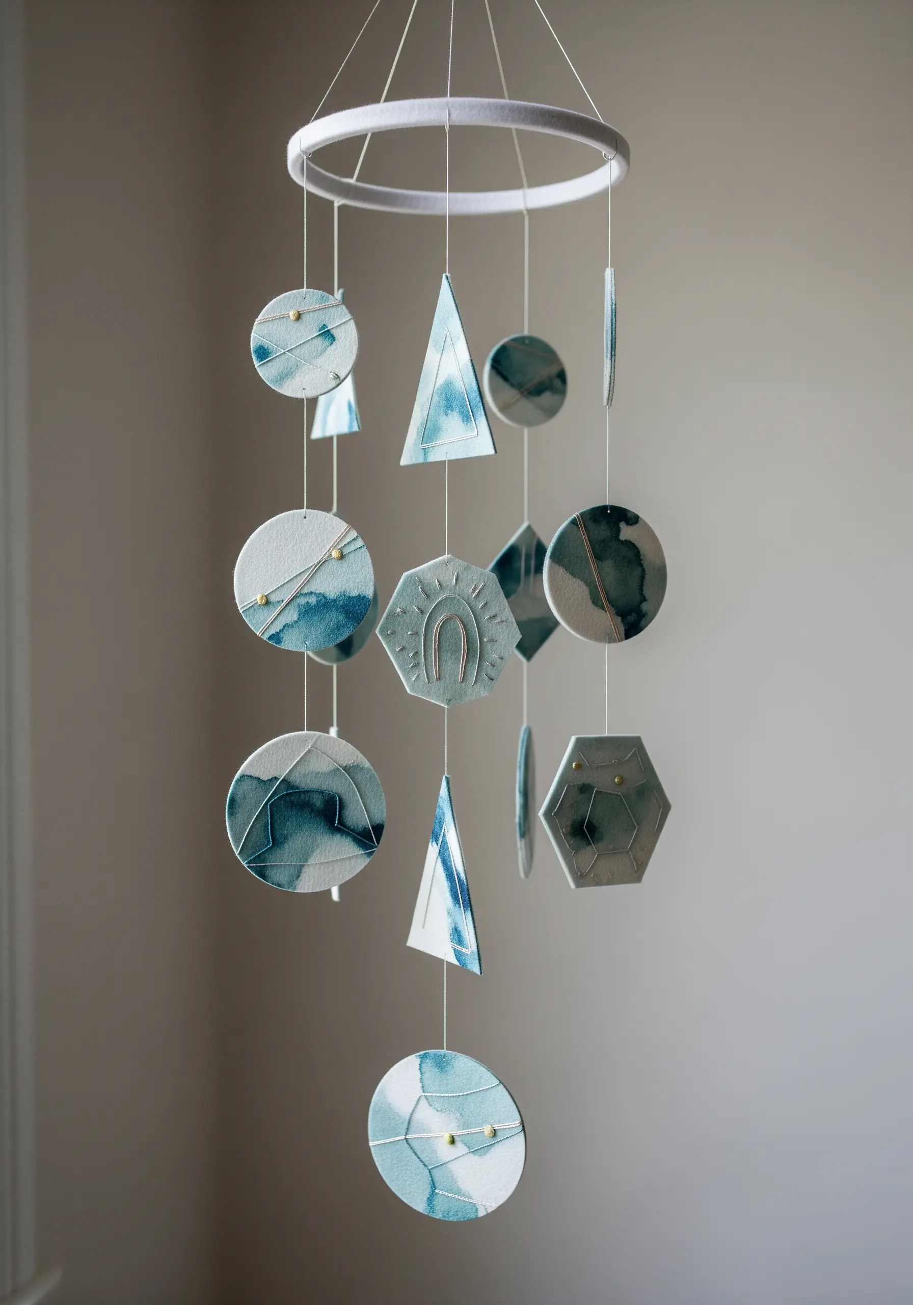 A nursery mobile with geometric watercolor paper shapes accented with gold thread and beads.