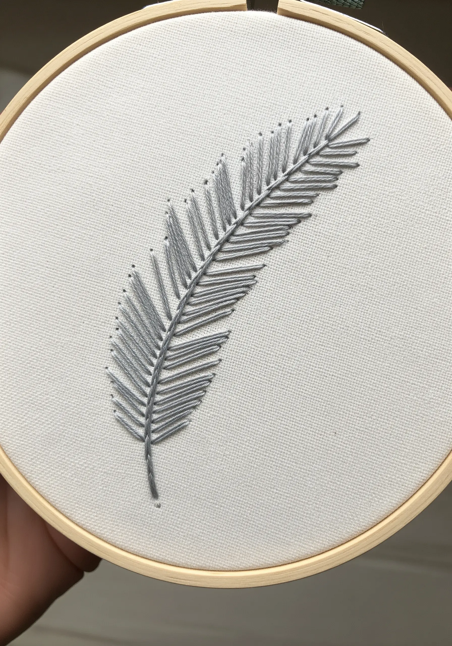 A delicate feather embroidered in gray thread with open, parallel straight stitches.