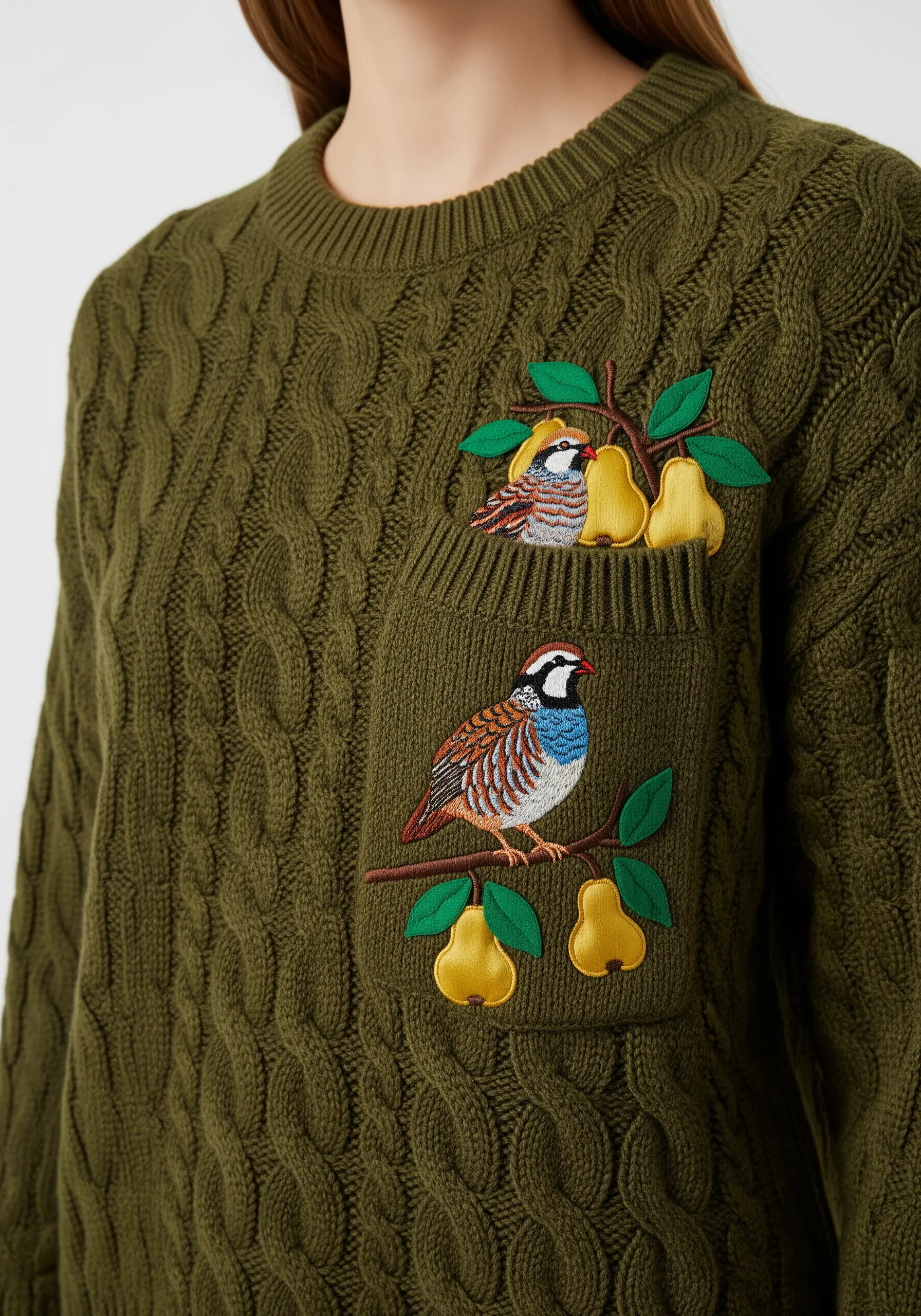 Embroidered partridge and appliqué pears on the pocket of a cable-knit sweater.