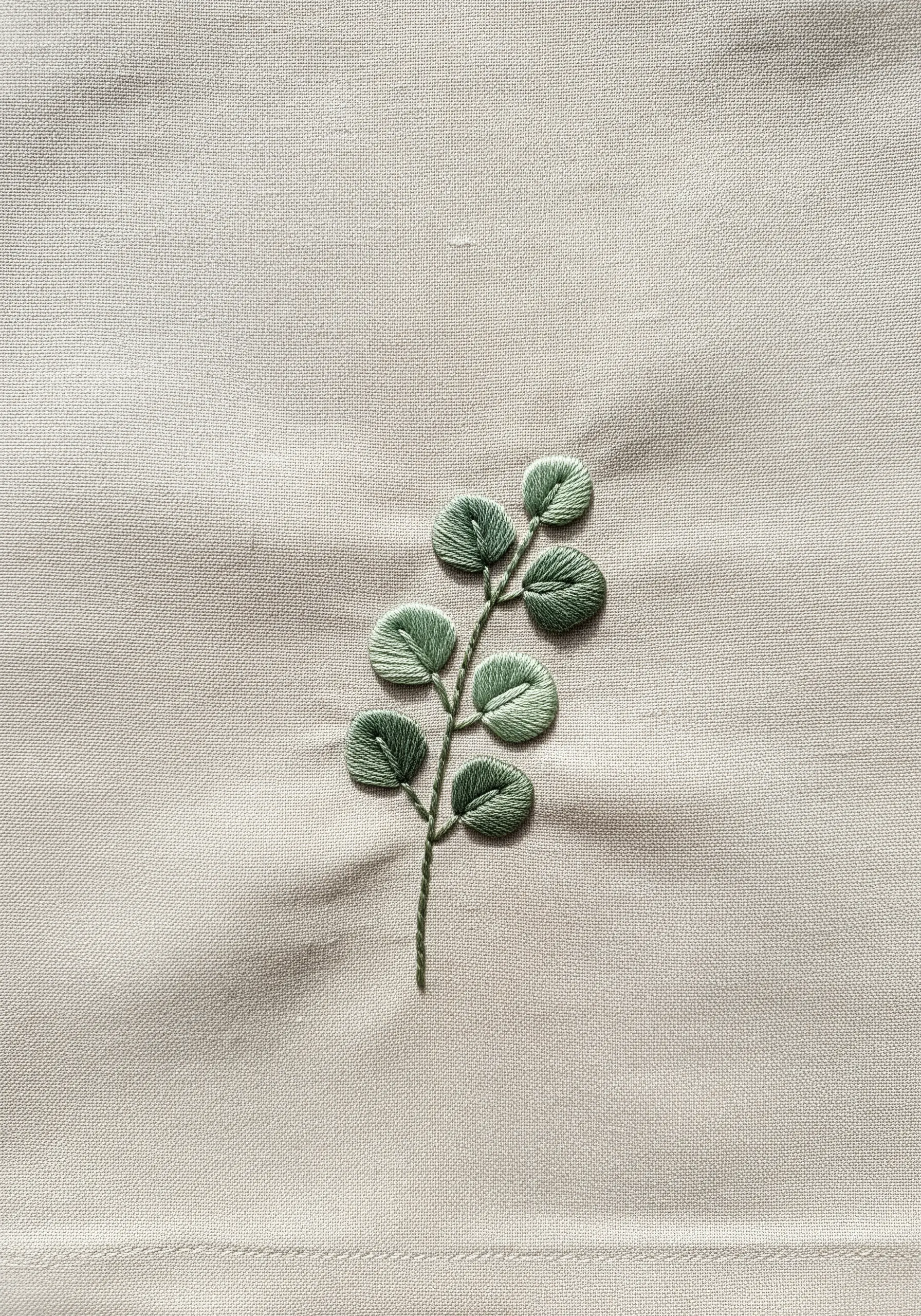 Satin-stitched eucalyptus leaves on neutral linen fabric.