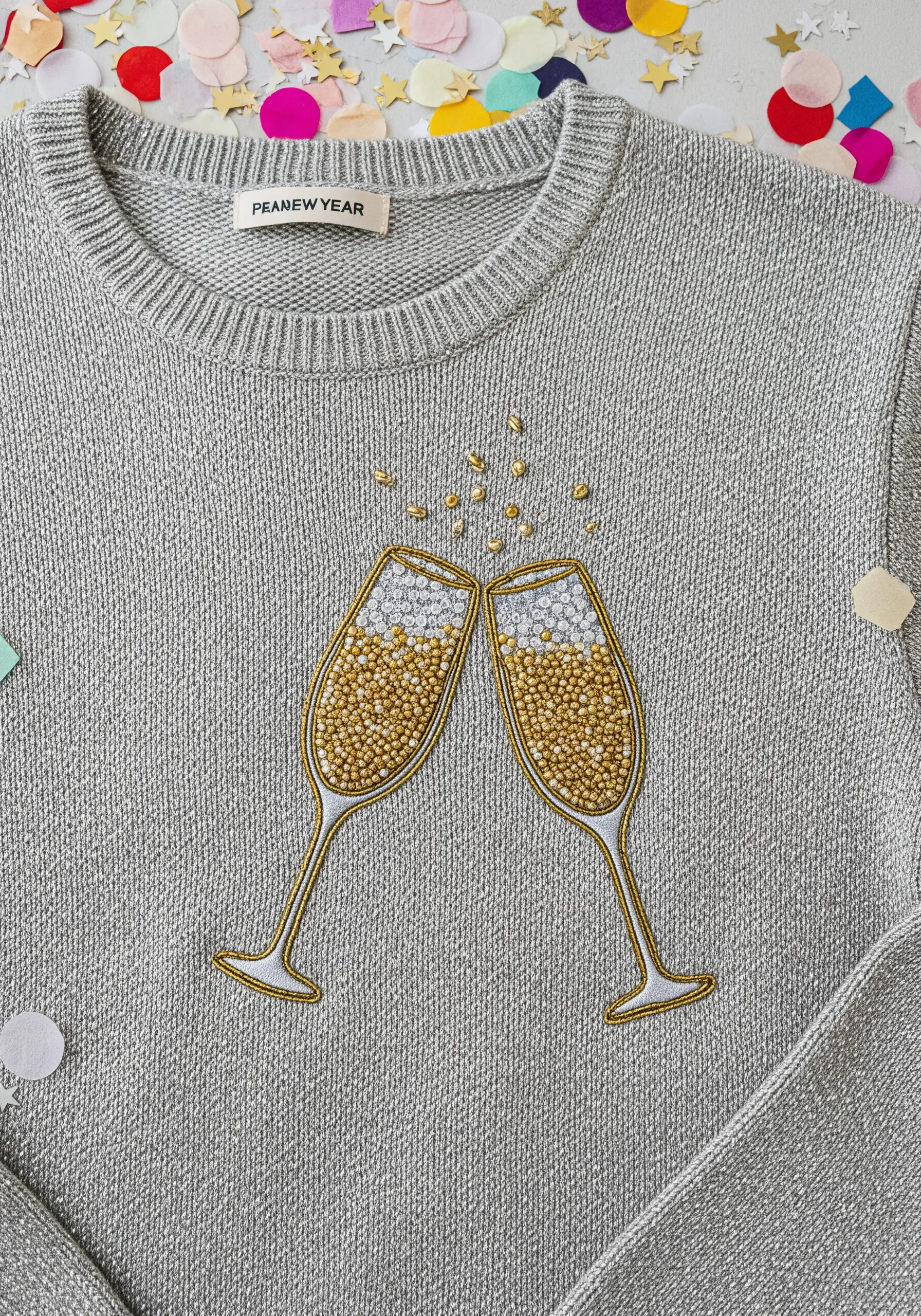Two champagne glasses filled with gold and silver bead embroidery on a silver sweater.