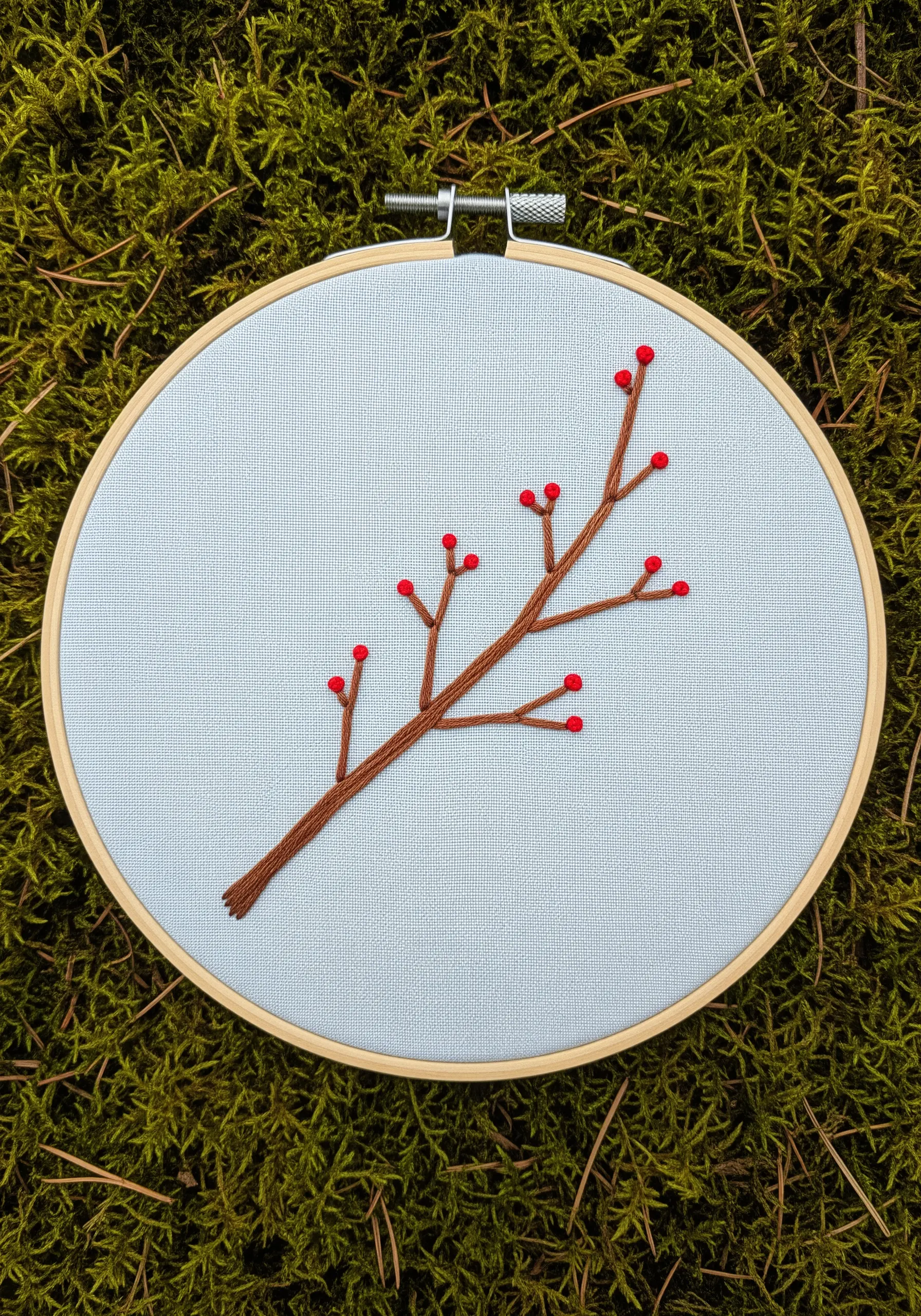 A simple embroidered branch with red French knot berries on blue fabric.