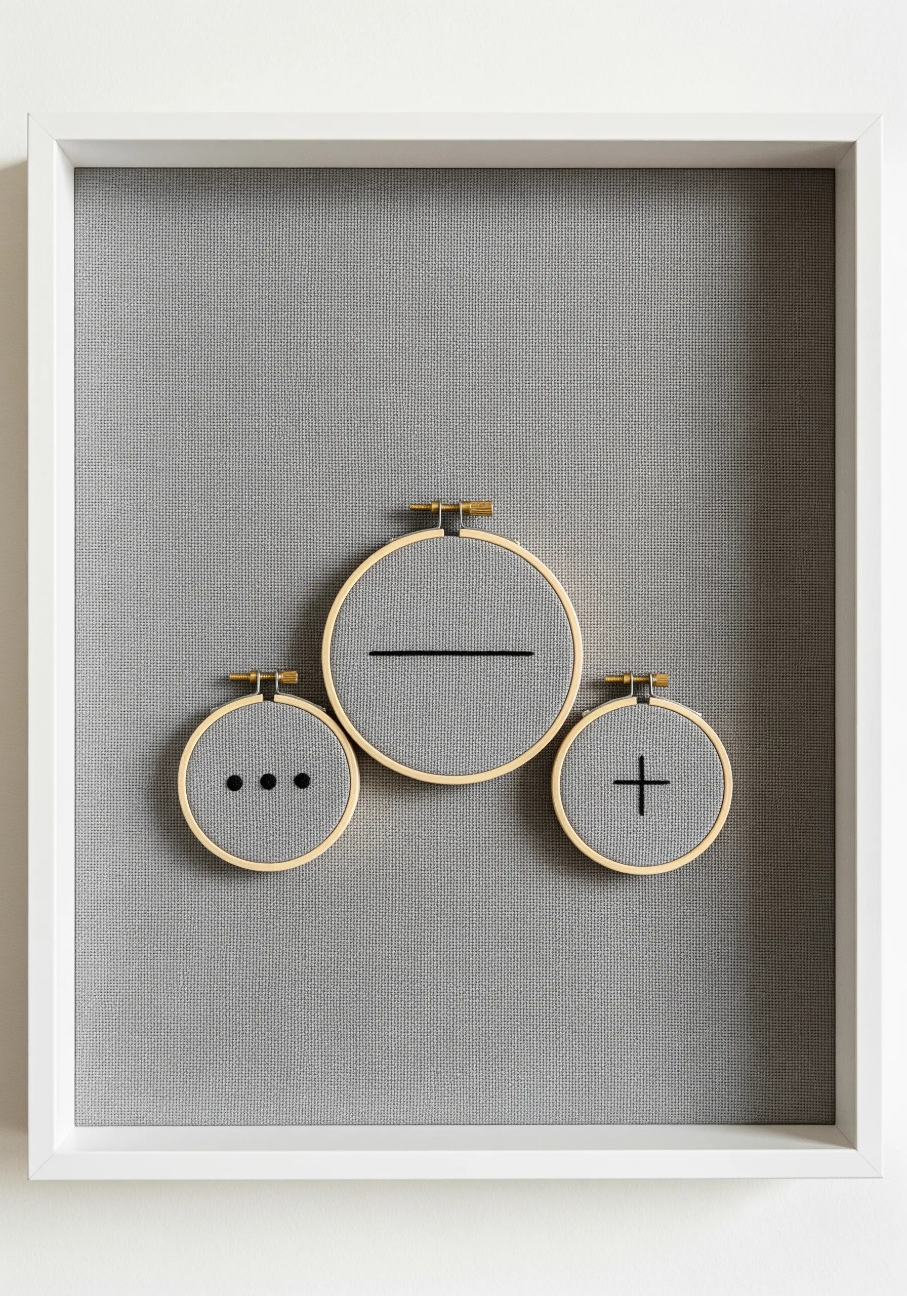 Three small hoops with minimalist symbols framed together in a large white frame.