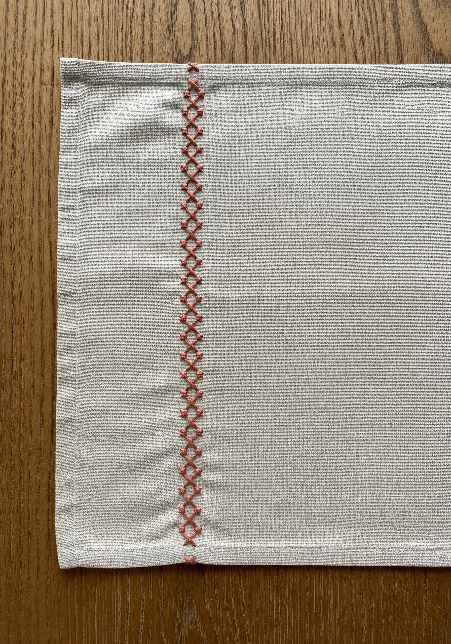 A decorative border in orange herringbone stitch on a neutral linen placemat.