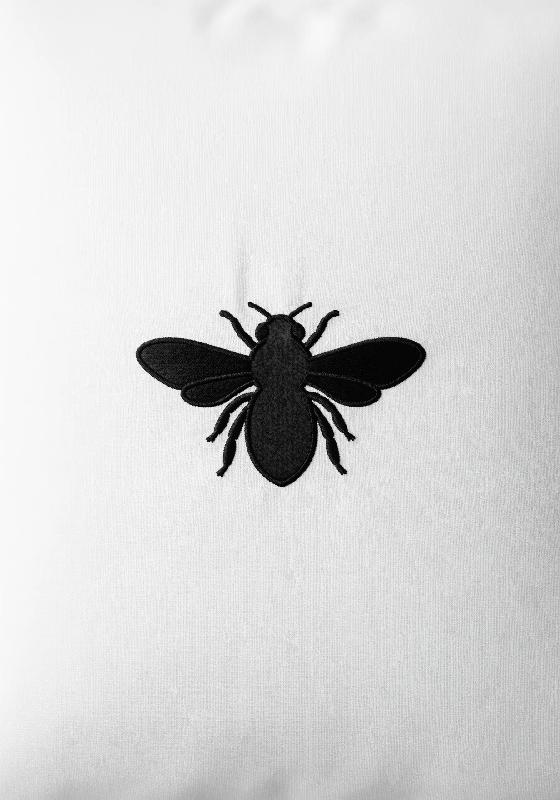 A solid black bee embroidered in a raised padded satin stitch on white fabric.